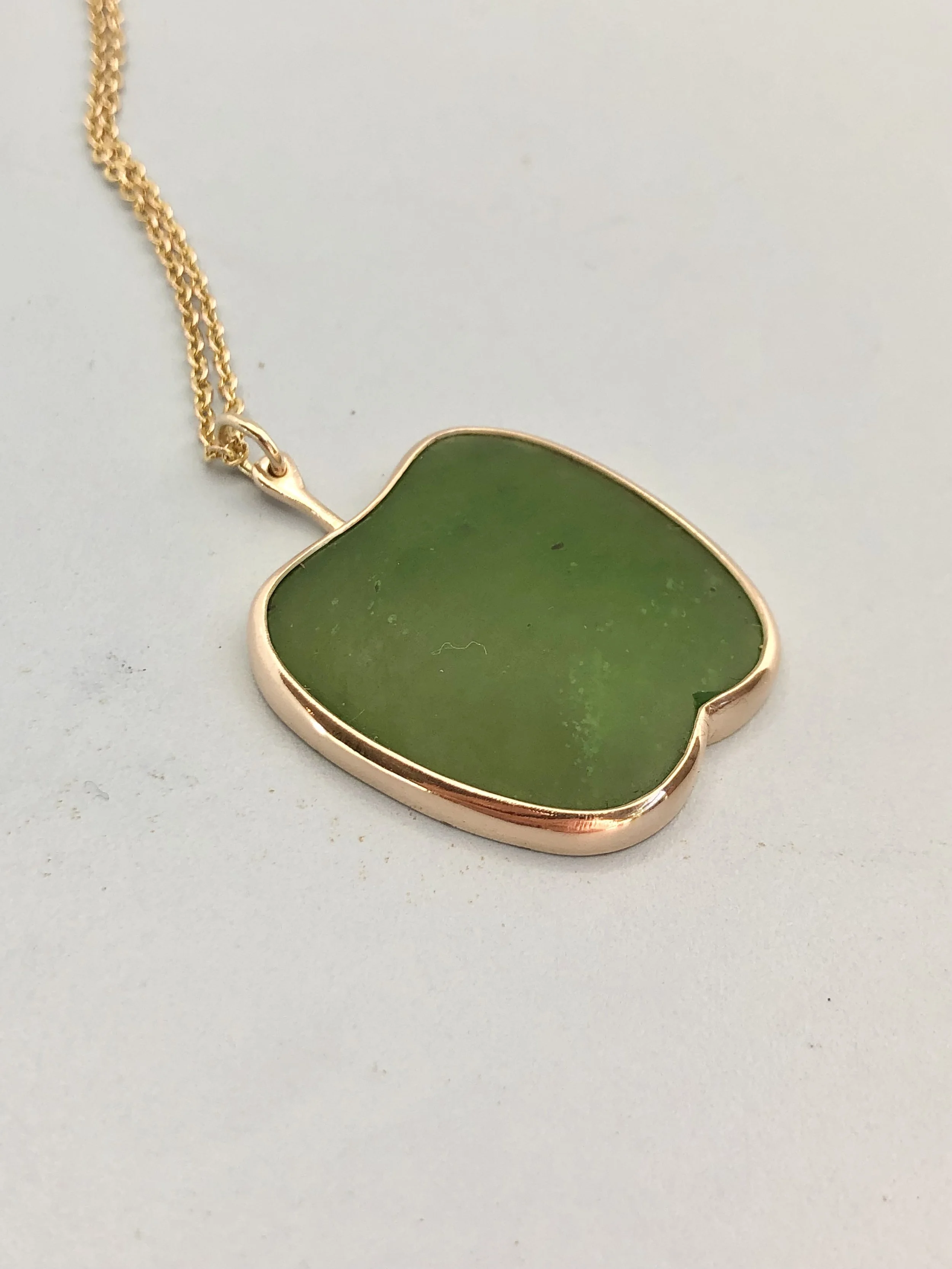 Pounamu apple pendant shown lying down from side view