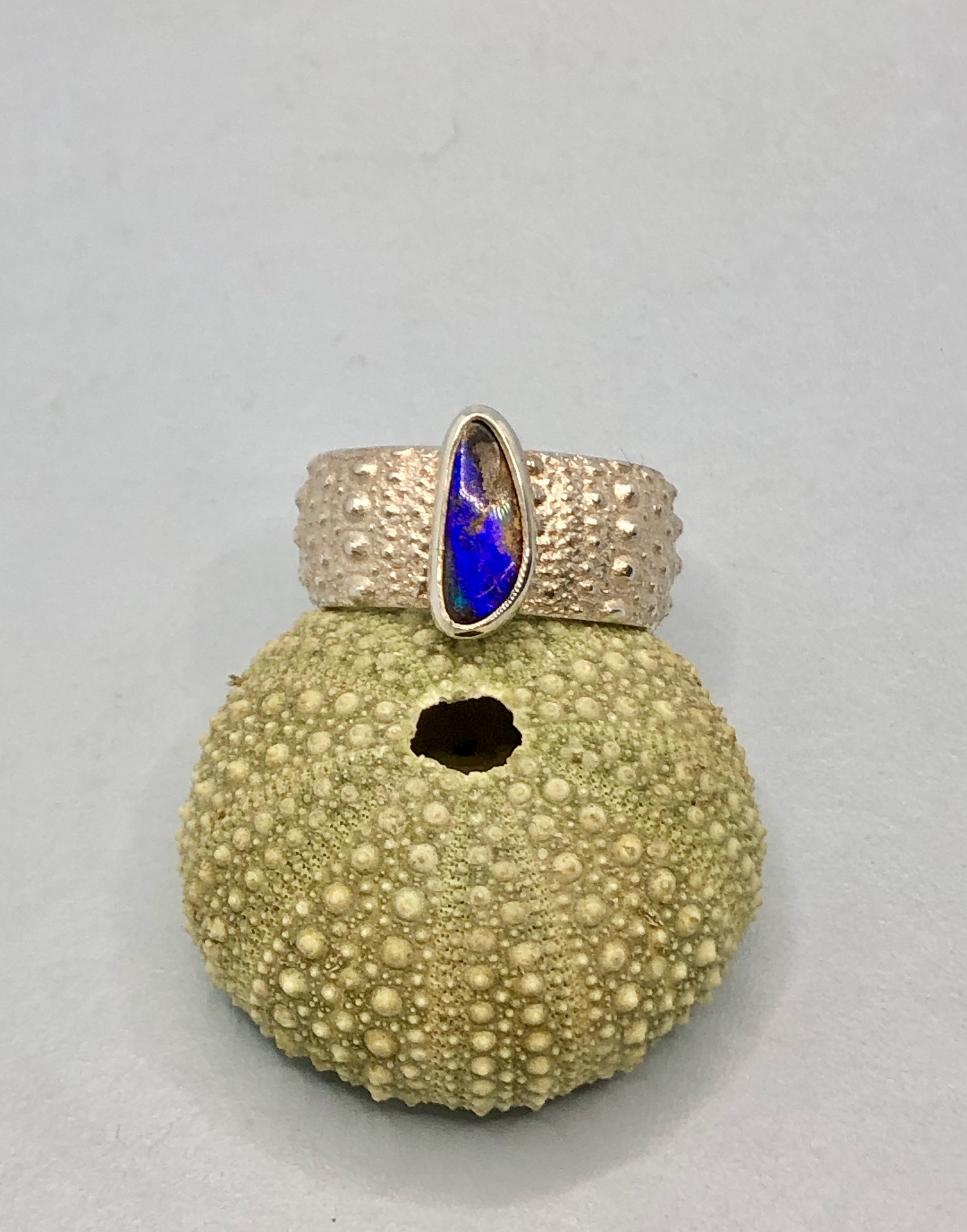 Front view of kin ring with Australian opal set on top, next to sea urchin to show pattern