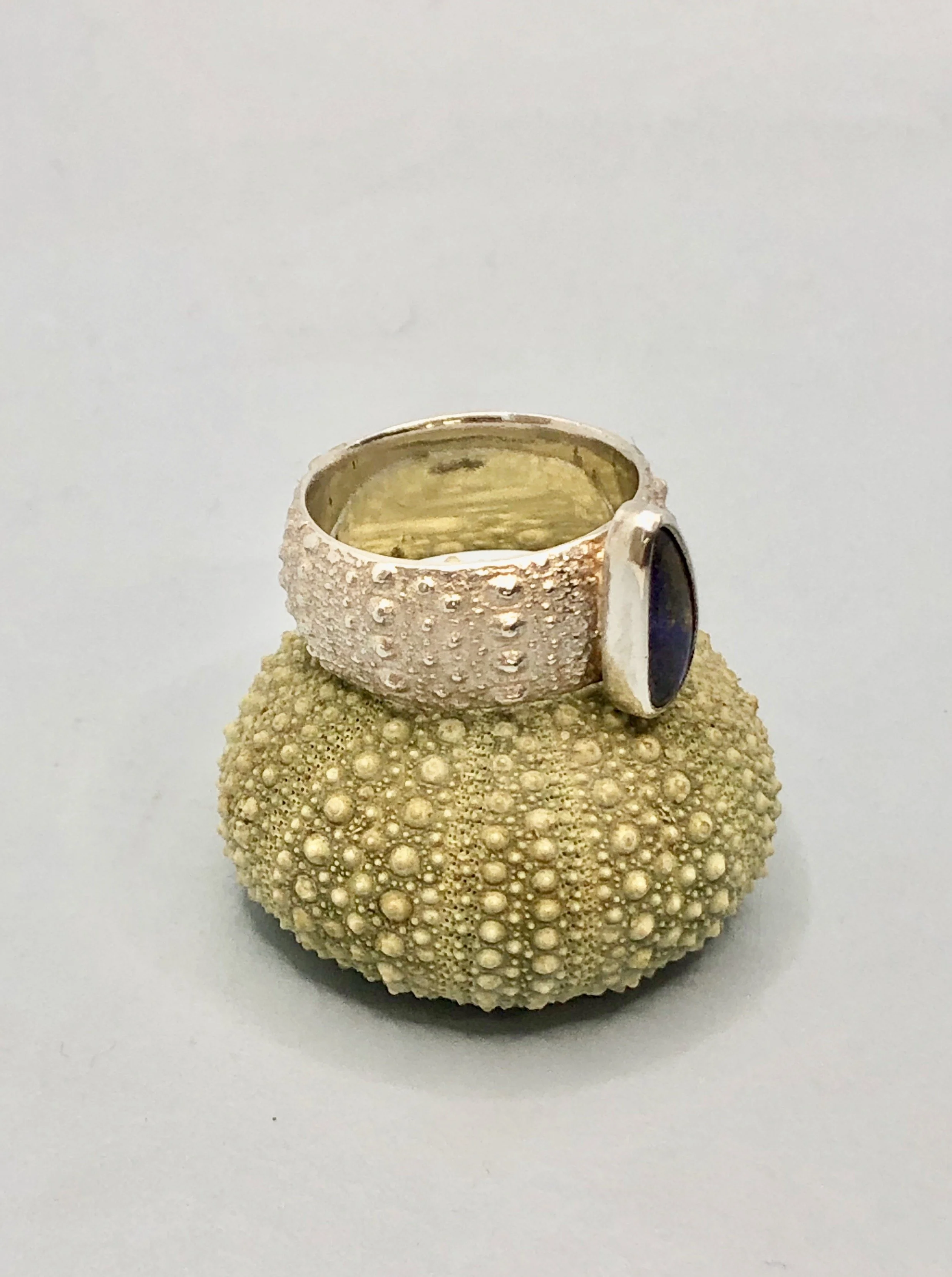 Side view of opal and silver ring on top of a Kina shell to show texture comparison