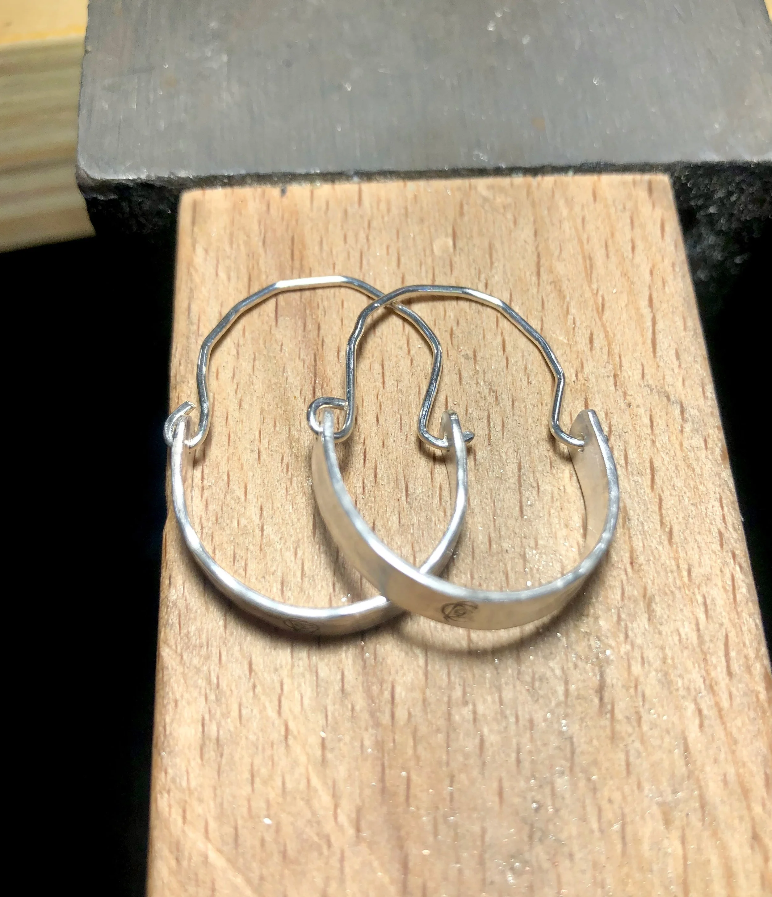 Sterling silver textured half hoop earrings with silver half hoop hook, sitting on a bench peg of a jewellers workbench