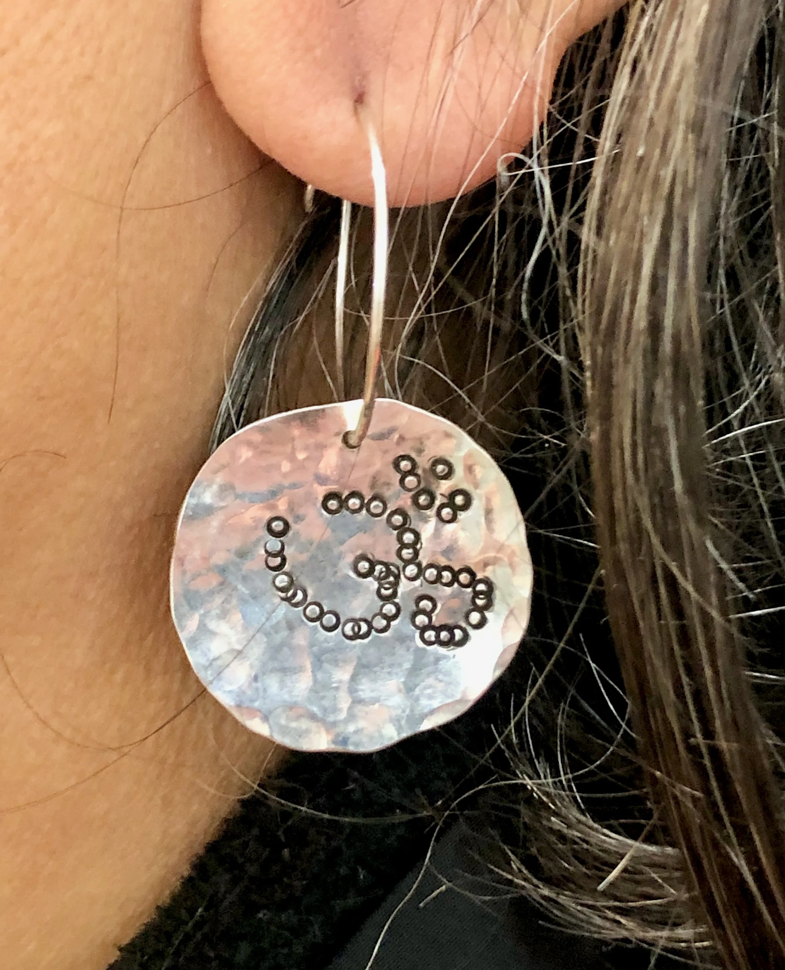 Hammer textured silver disc earrings with omshanti pattern impressed into the 925 silver, worn on the jewellery maker