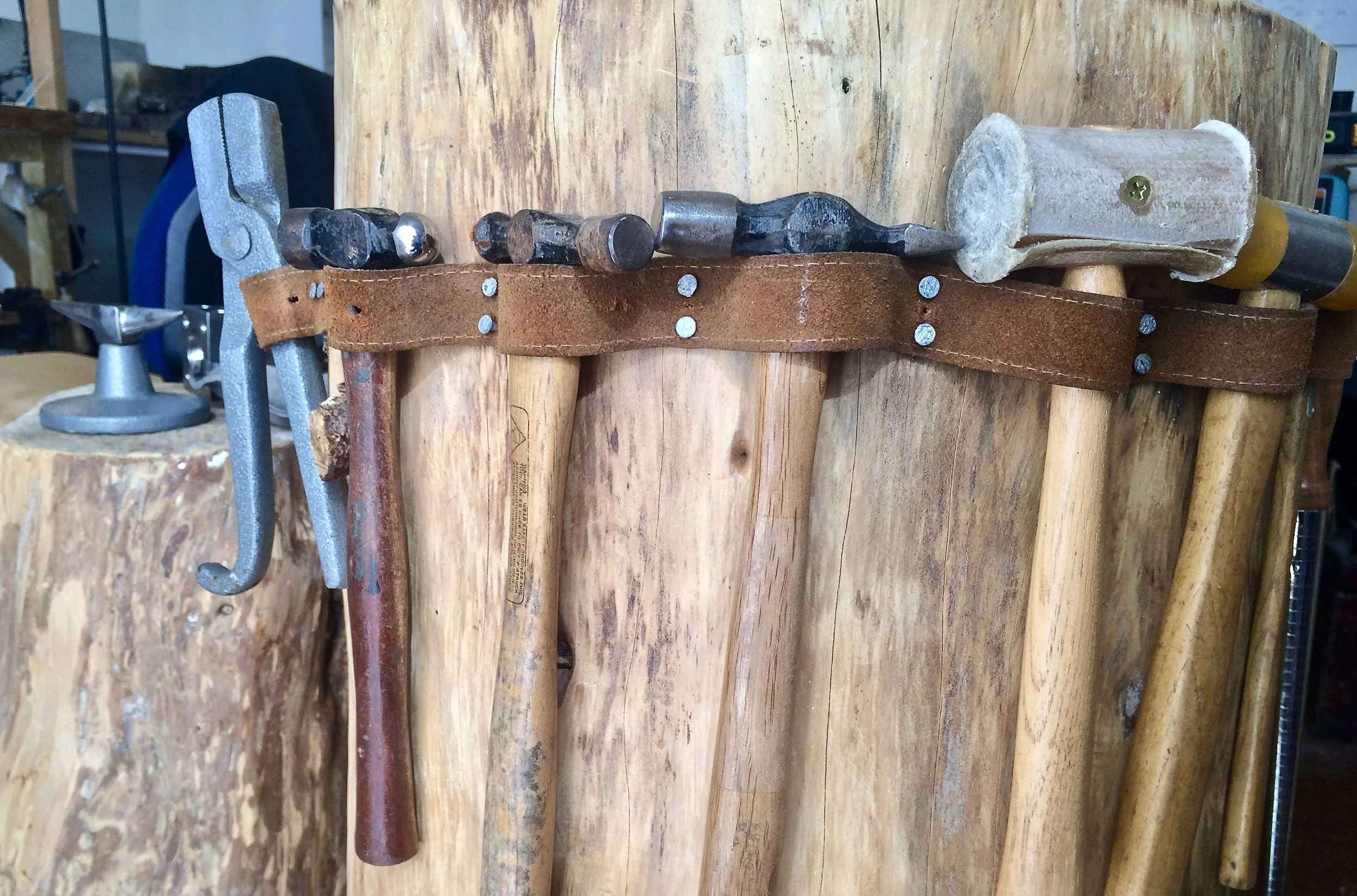 Jewellery making hammers and mallets resting on a wooden stump, essential tools for forming and texturing silver and copper.