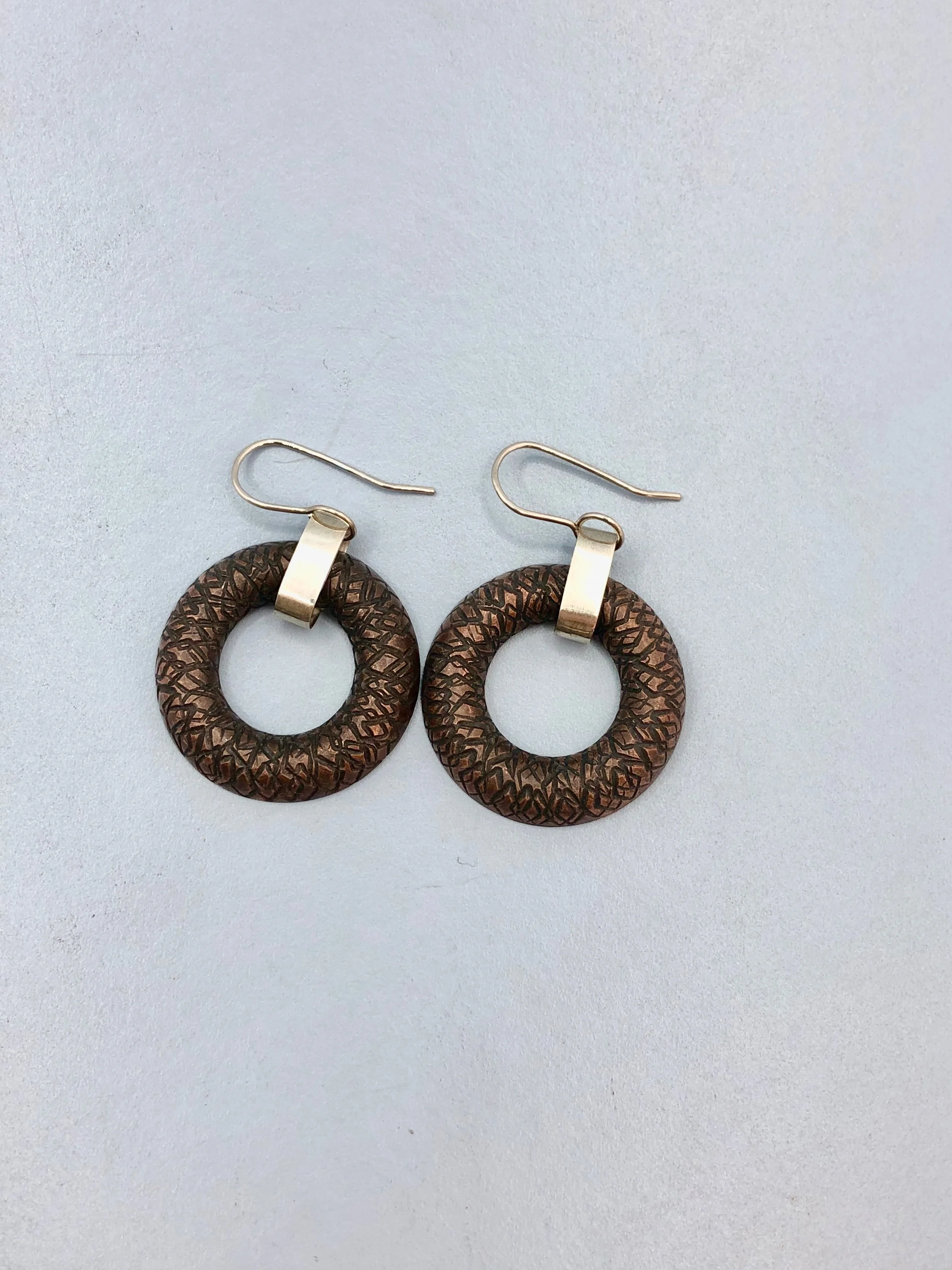 Front view of earring lying down, showing textured copper donut shape and sterling silver chain link and ear hook
