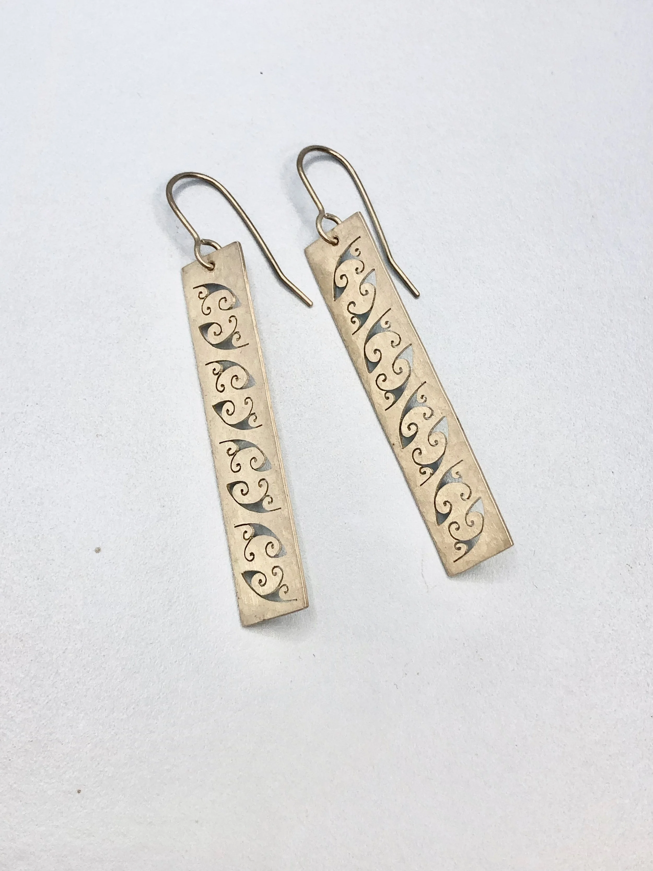 Hand cut koru pattern earrings shown lying on their side.