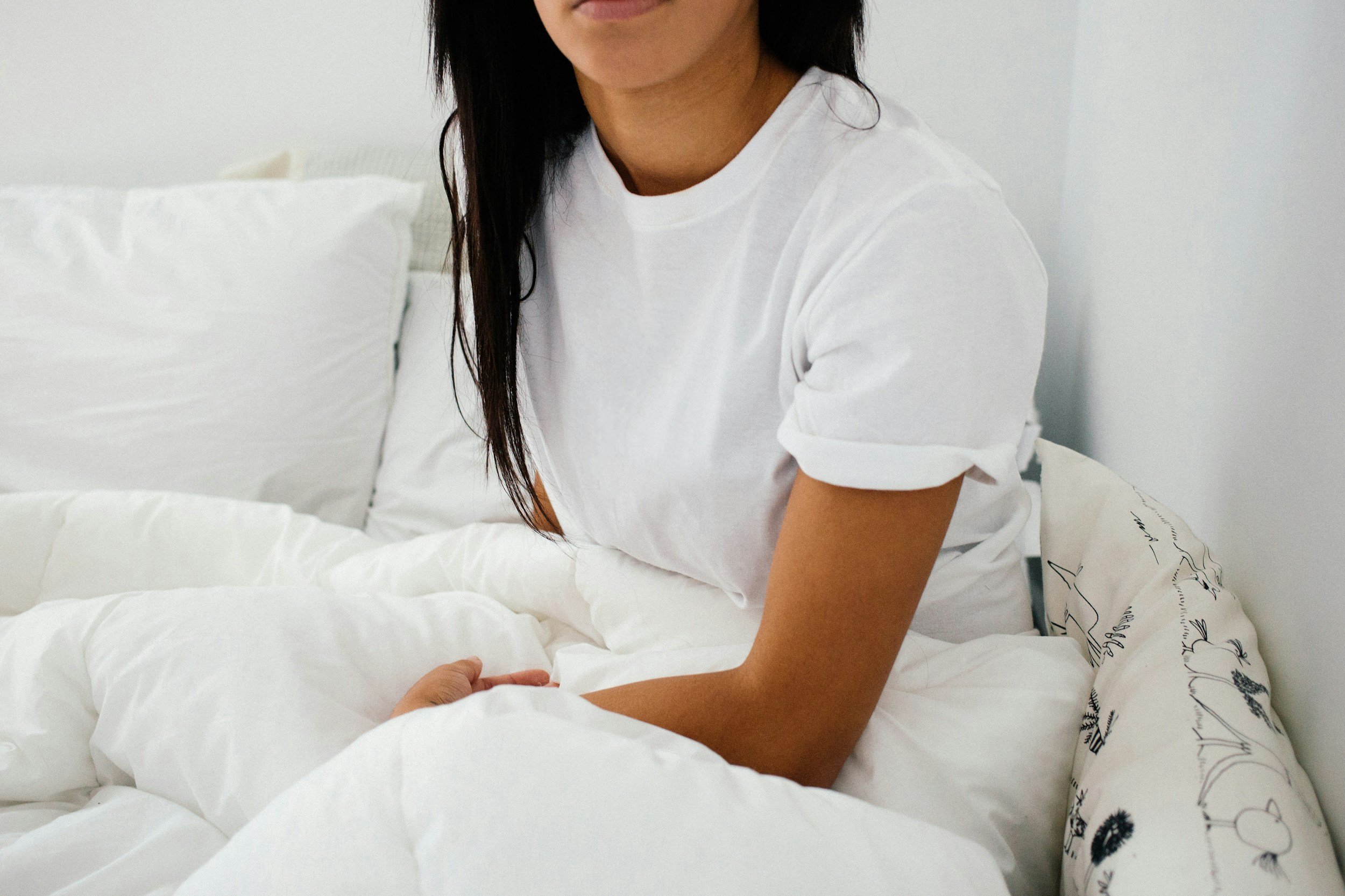 a woman in a white tshirt sitting in bed with a white duvet,  what is self worth, low self esteem