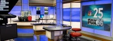 Television news studio with a desk, chairs, and screens displaying the NBC 25 FOX 66 logo.