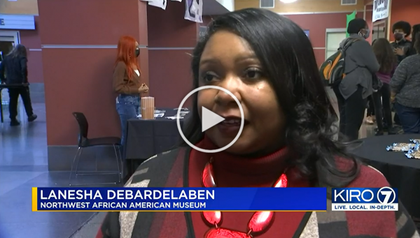 Close-up of Lanesha Debardelaben speaking at an event, with other attendees and booths in the background at the Northwest African American Museum.