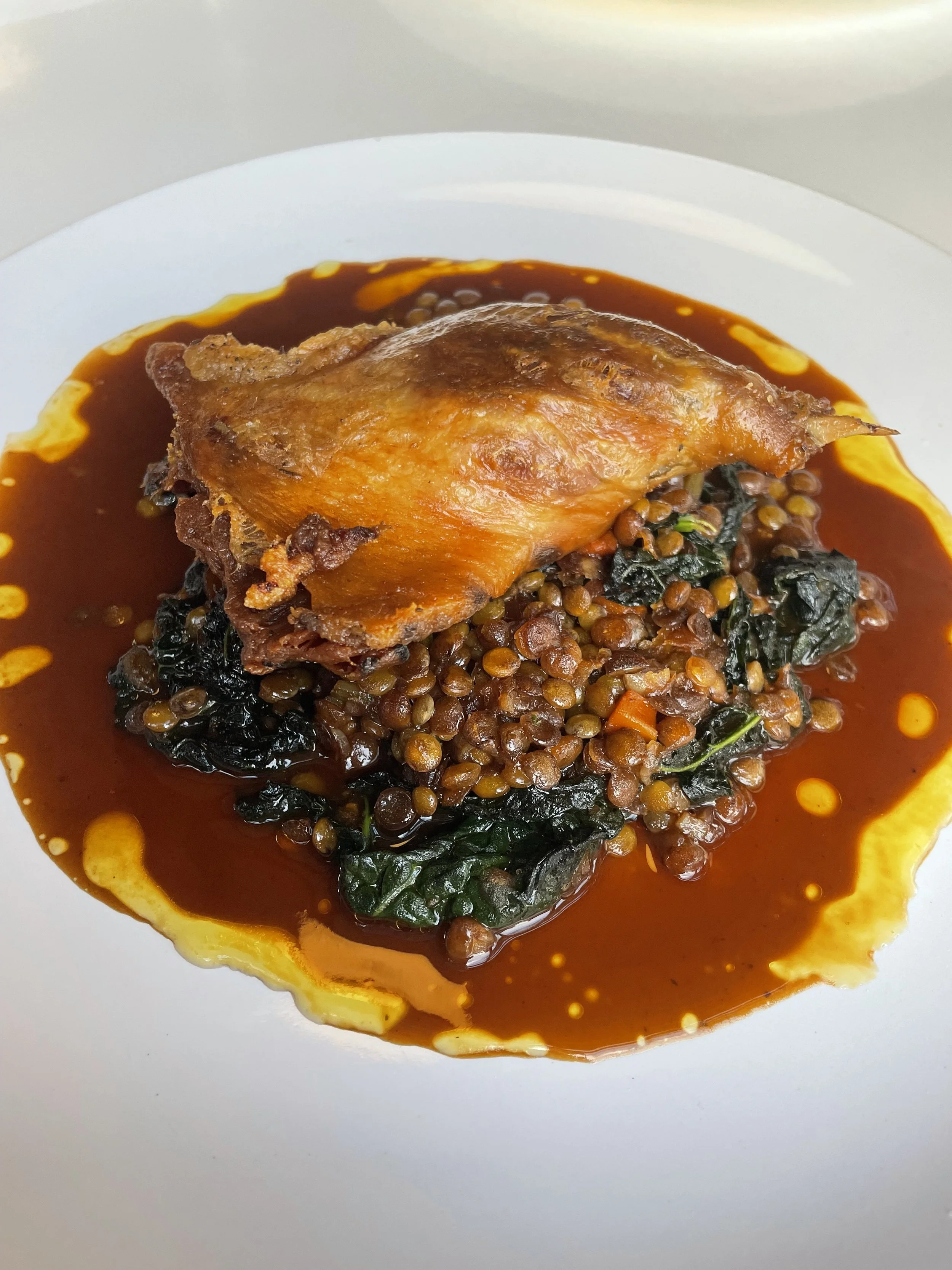 A plate of cooked collard greens, lentils, and a roasted chicken thigh with gravy.