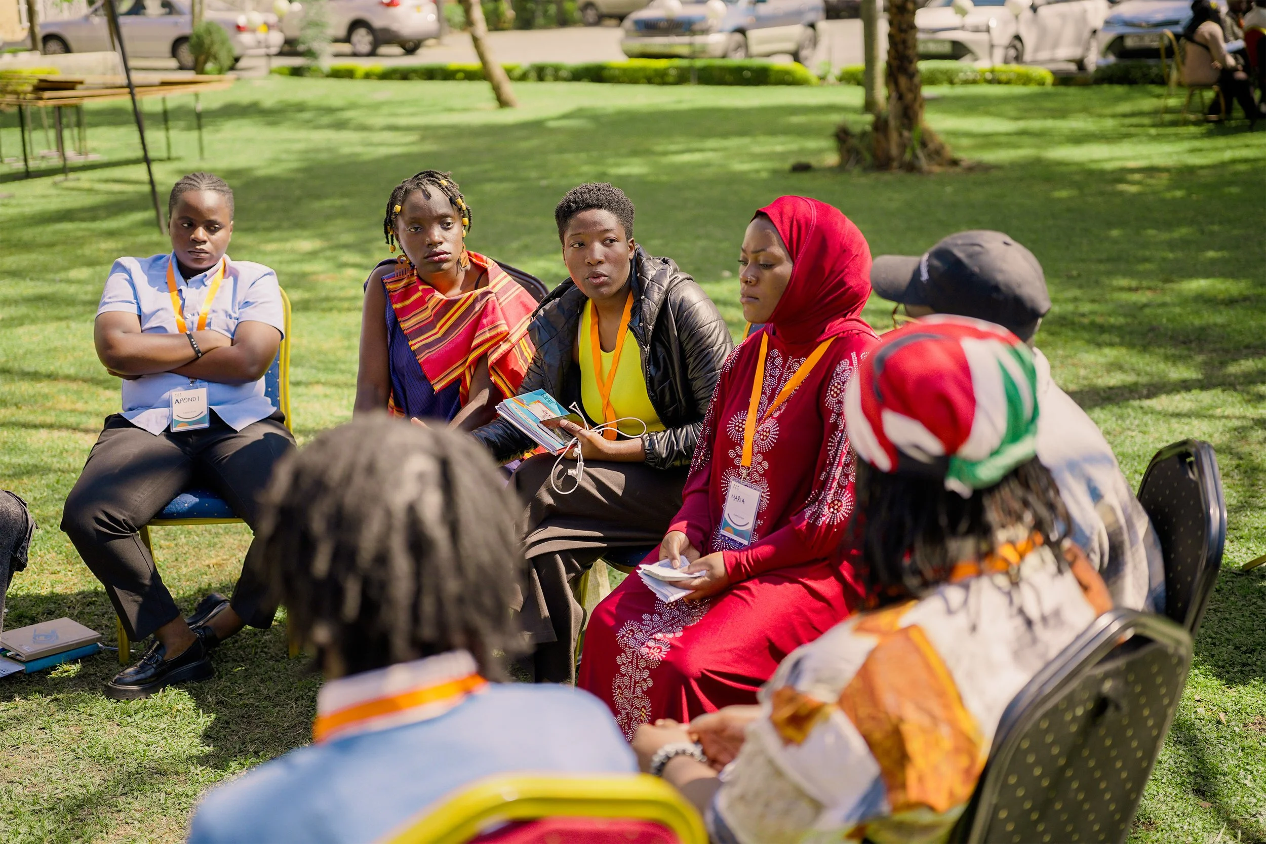 A group of young diverse women sat in a circle outside in a workshop session.
