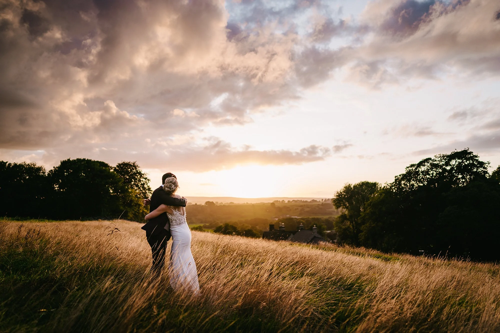 A couple hugging in a grassy field at sunset.