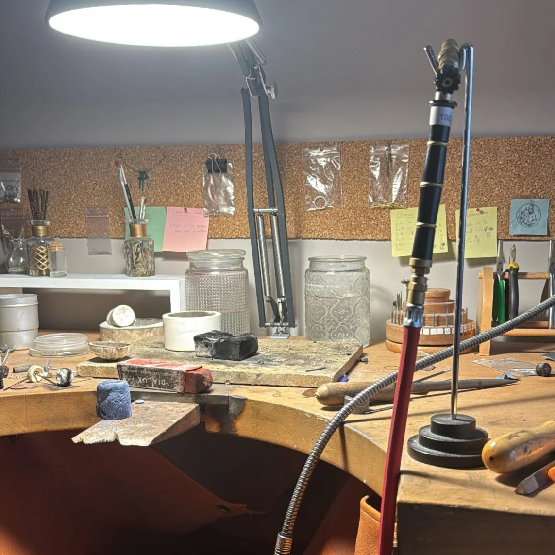 Un atelier de bijouterie avec des outils et des matériaux sur un plan de travail en bois, éclairé par une lampe