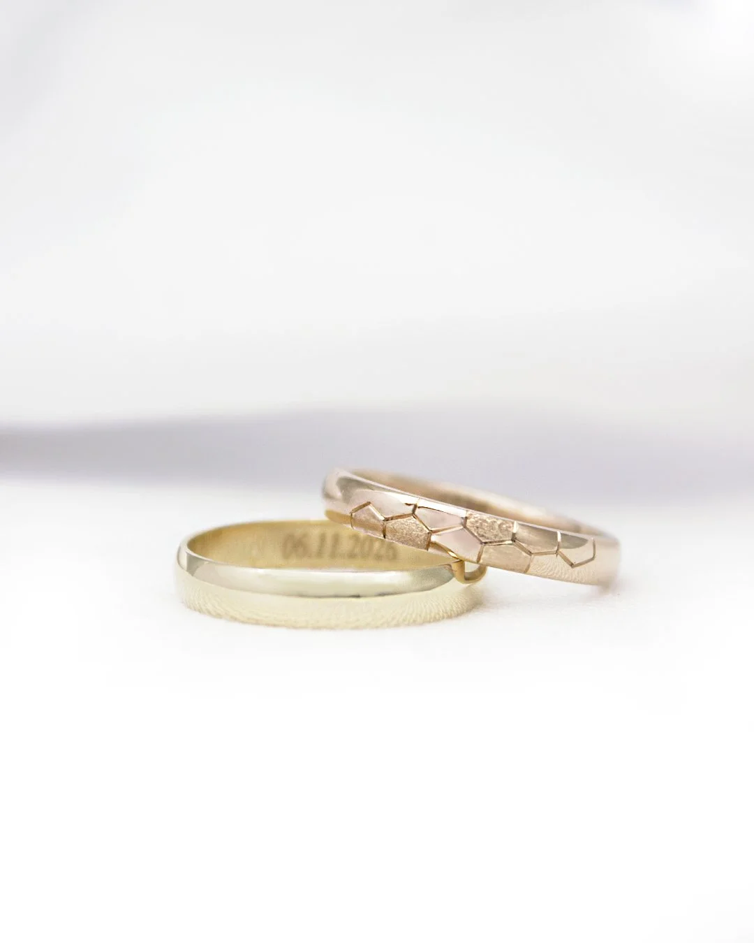 Deux alliances de mariage en or, l'une avec motif hexagonal et la seconde avec une texture simple, posées sur un fond blanc.