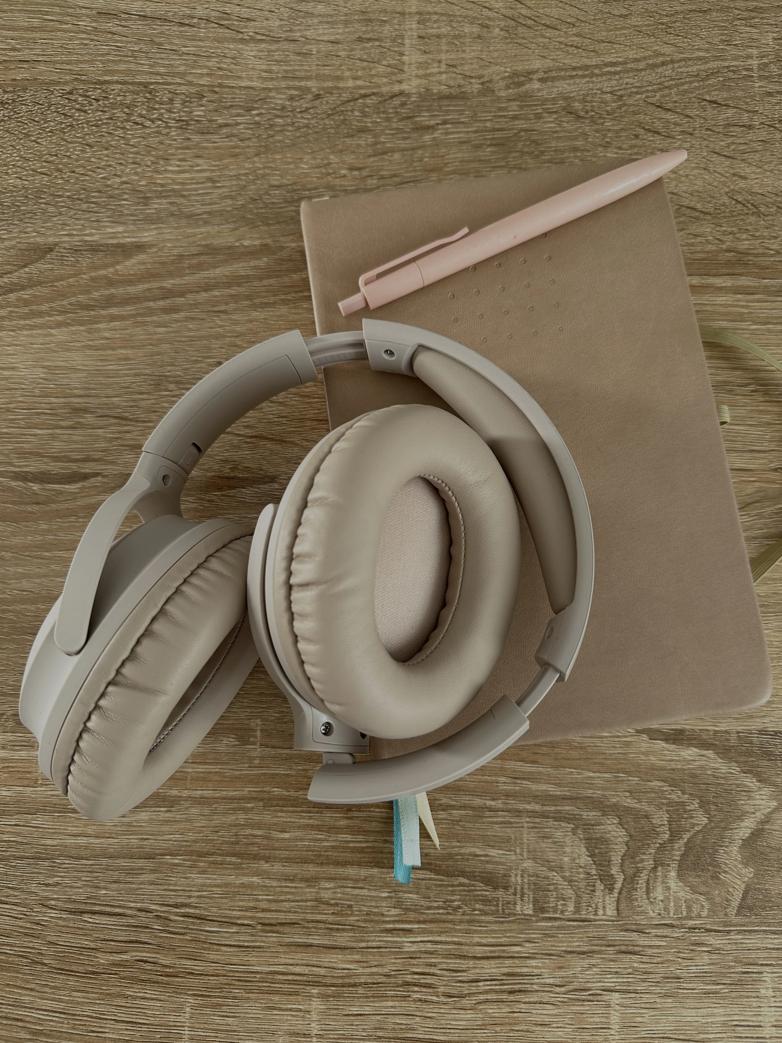 Beige headphones on top of a beige notebook. A beige pen is resting on the top of the notebook. This is linked to the "contact us" page.