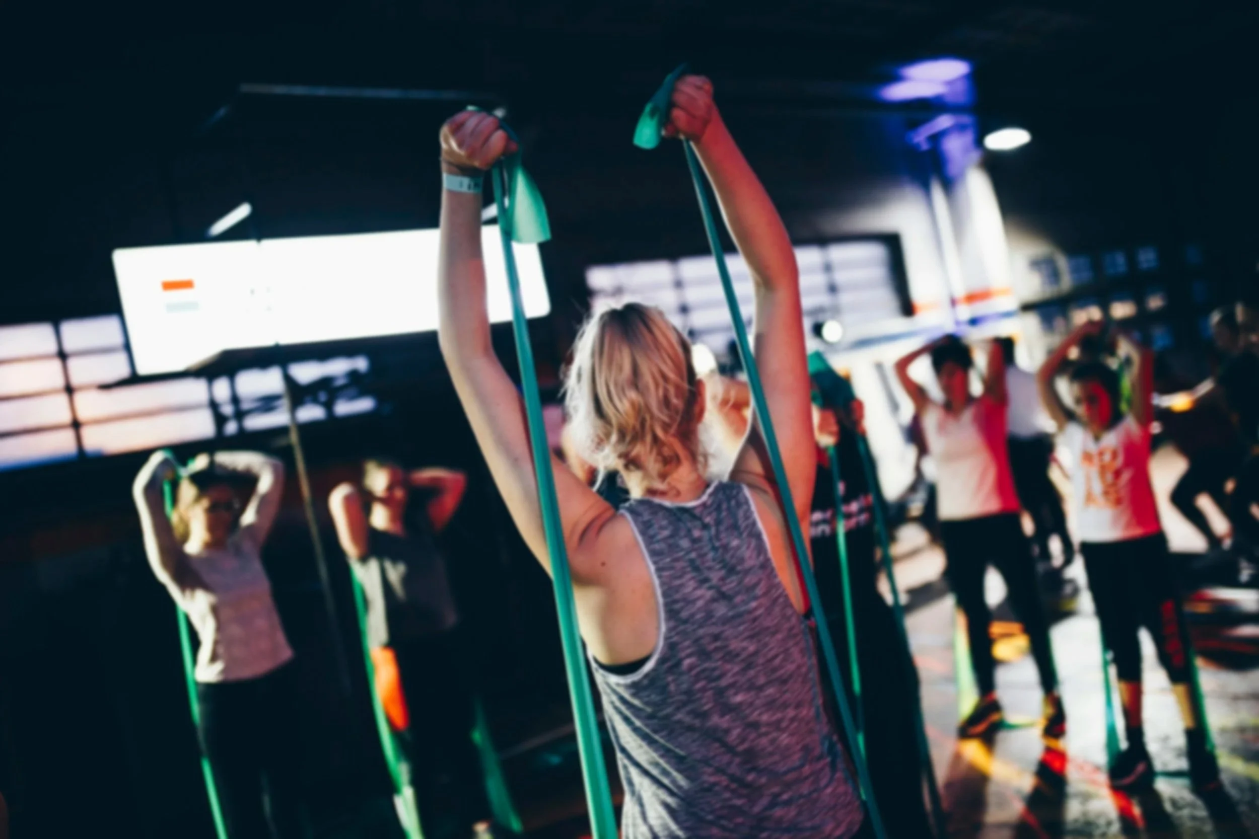 People participating in a group fitness class at a gym, using resistance bands for exercise.