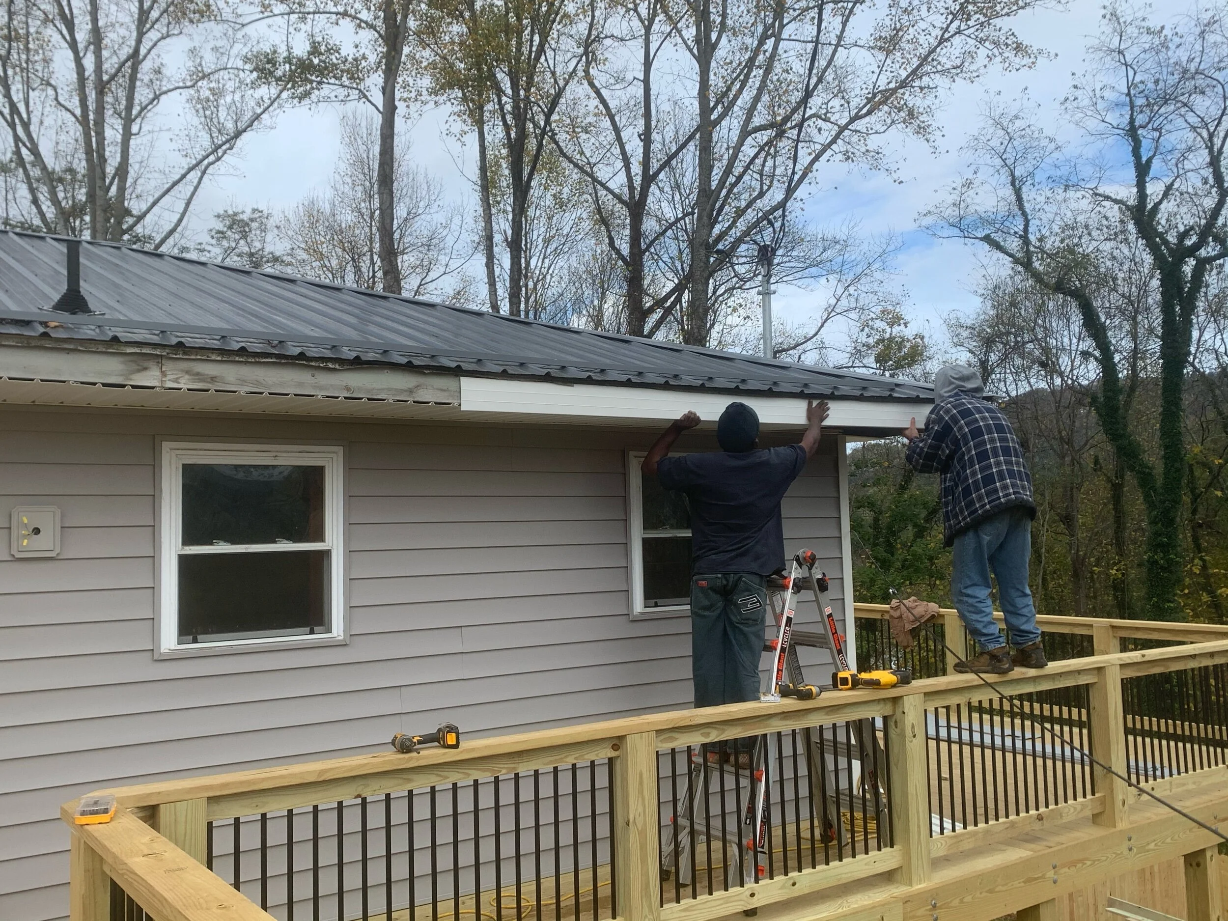 Two people working on installing gutter on a house roof edge.