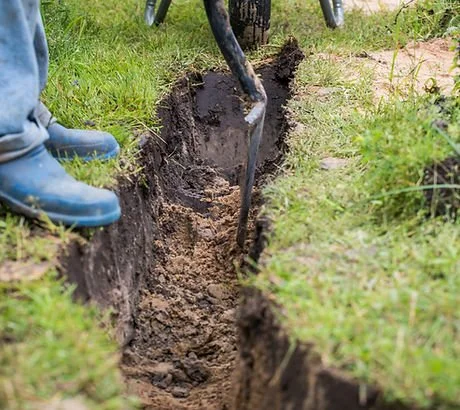 Person digging a trench with a shovel in a grassy area