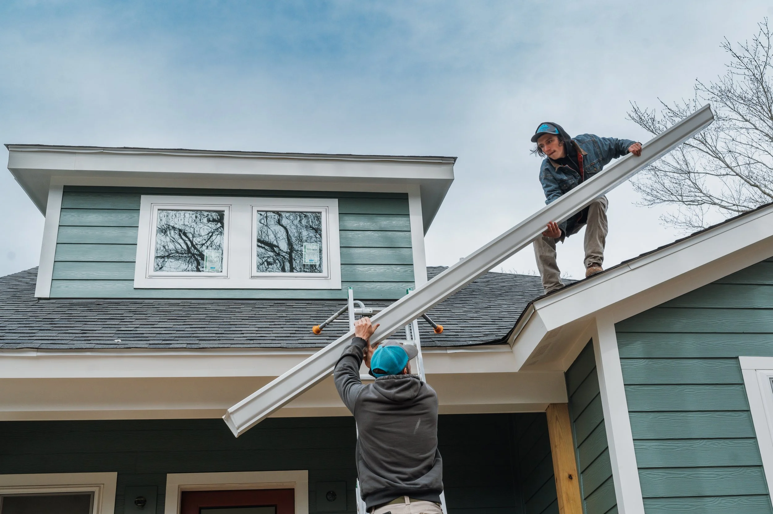Gutter installers passing a piece of custom fabricated seamless gutter onto the roof in Asheville, NC