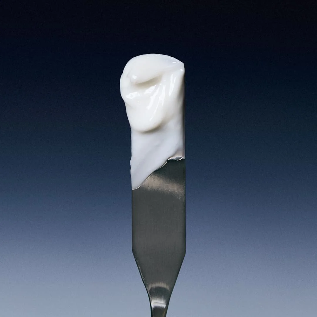 Close-up of a dental tool with a dollop of white toothpaste on its end against a dark background.