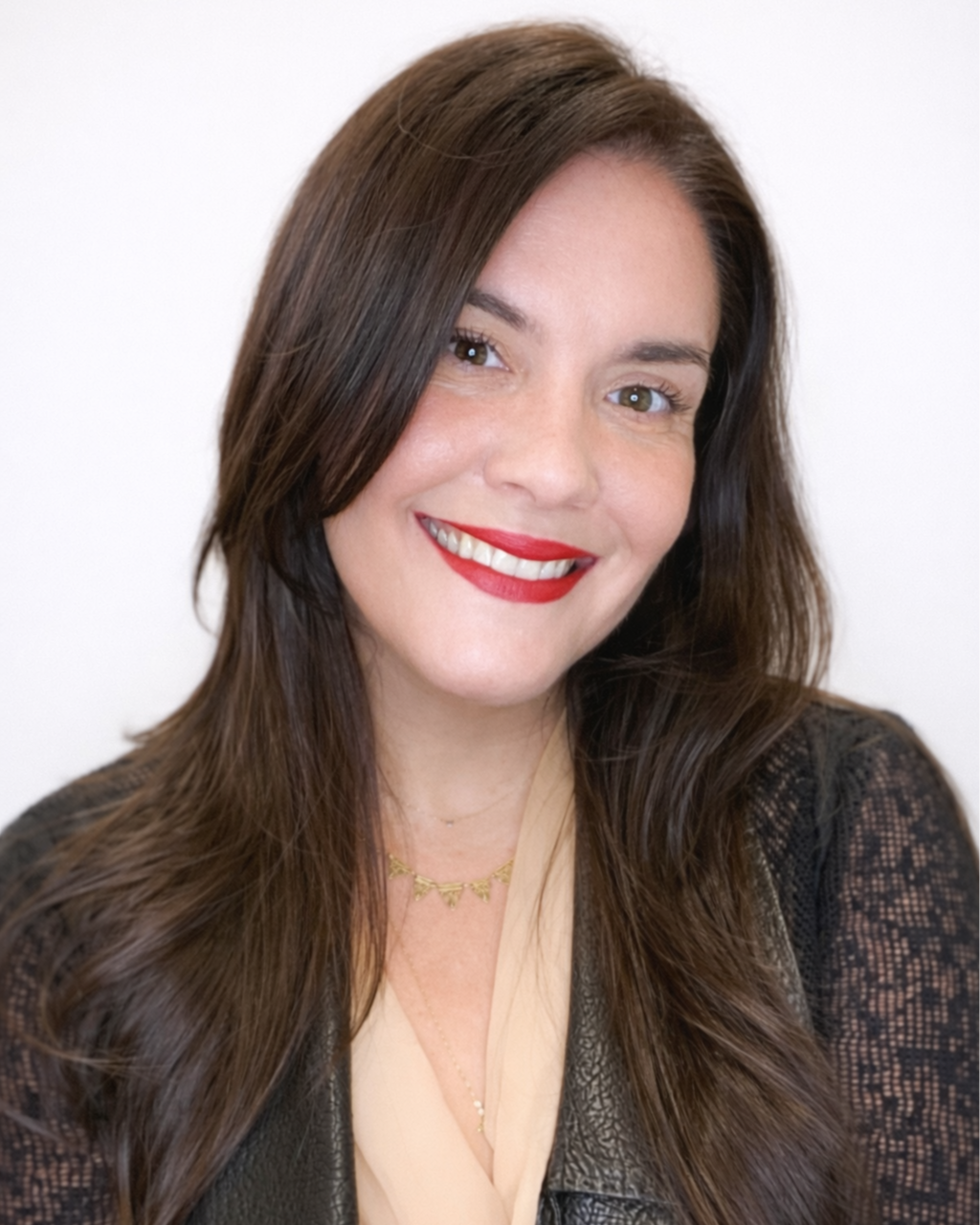 A woman with long brown hair and red lipstick, smiling, wearing a black lace top and gold necklace.