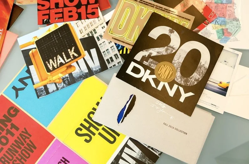 A collage of various fashion and event promotional materials, including posters, flyers, and cards, with designs and text such as 'SHOE FEB 15', '20 DKNY', and 'WALK' on a light surface.