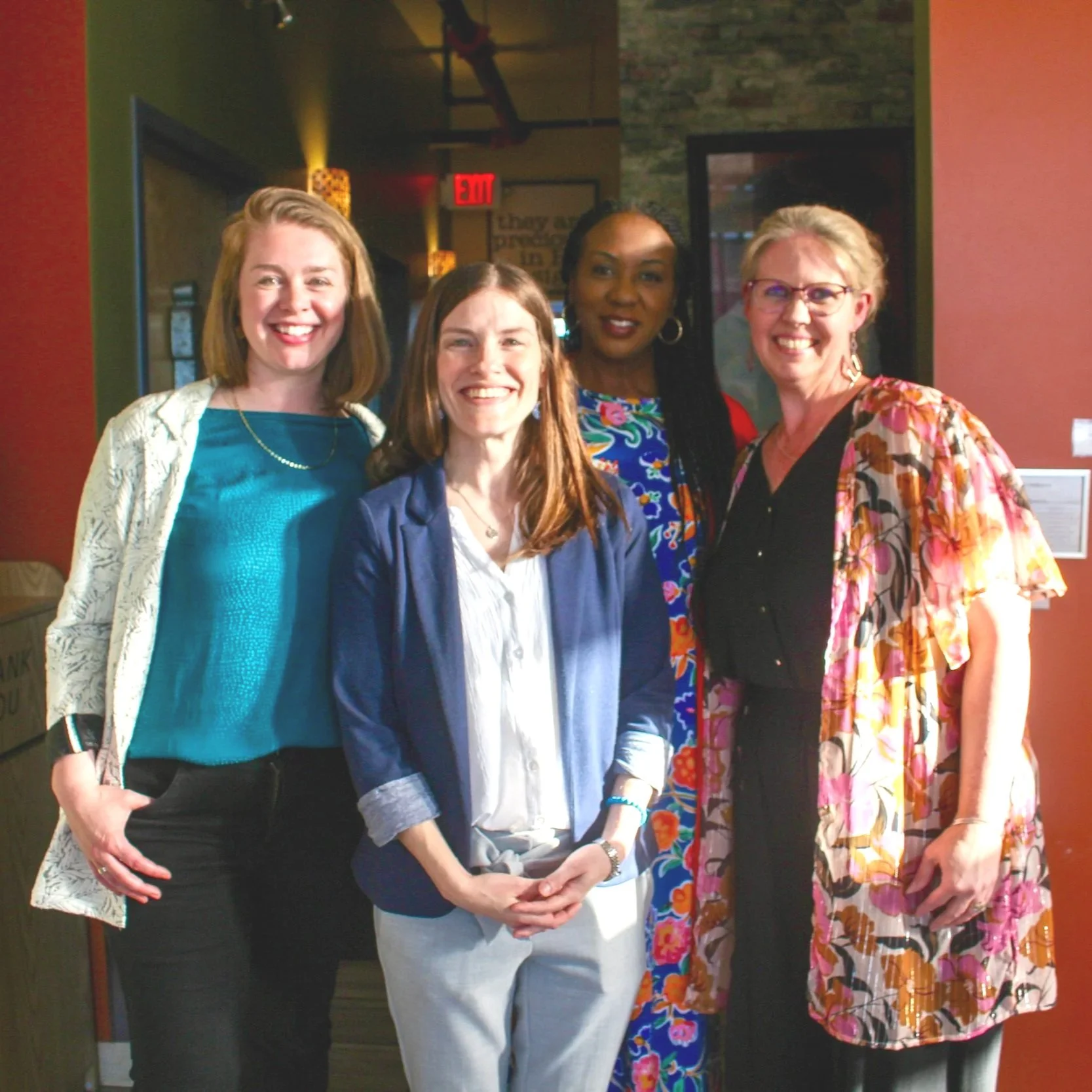 Four women standing inside a restaurant or café, smiling at the camera.