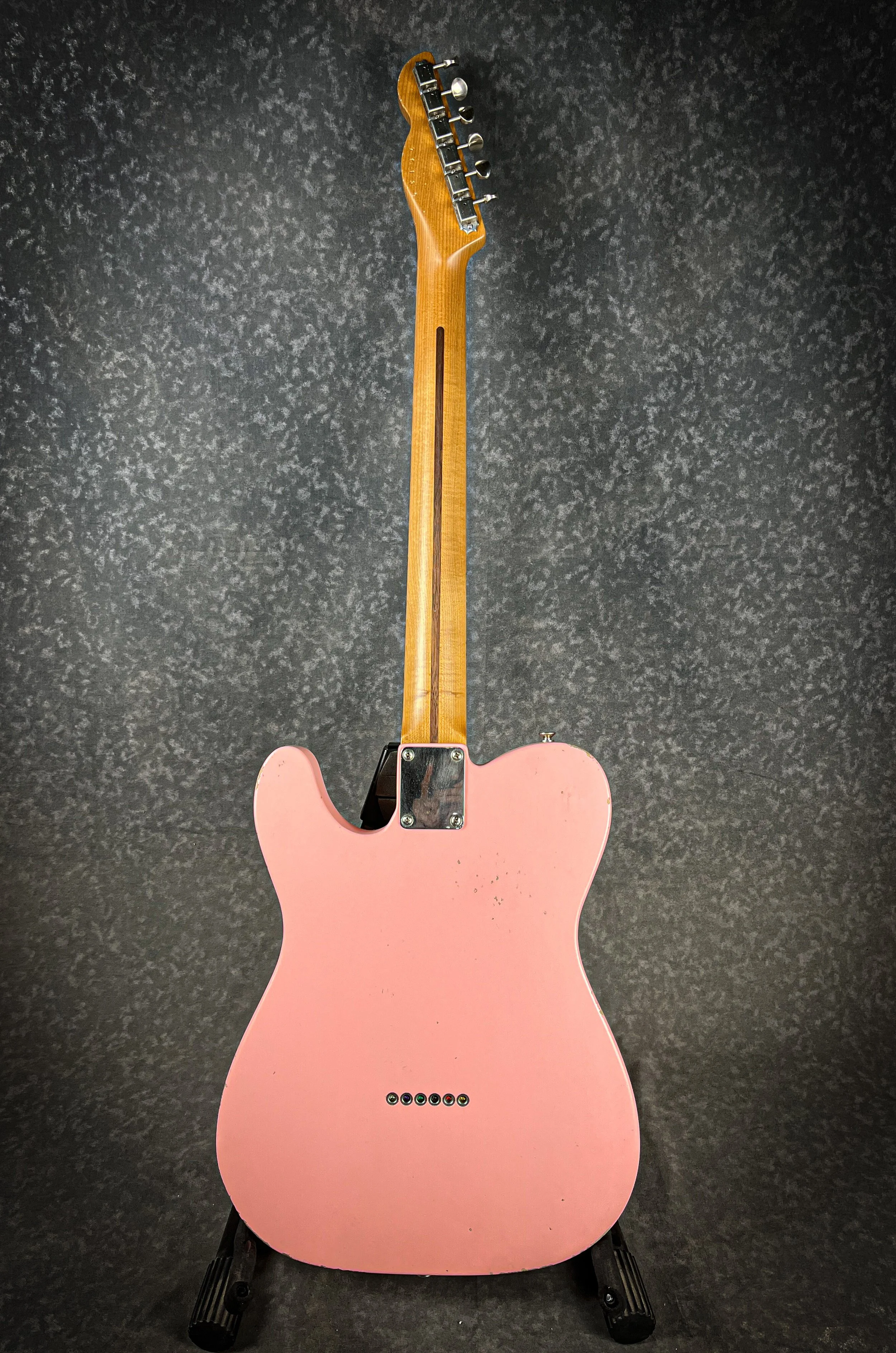 Back of a pink LSL T Bone electric guitar on a black stand against a black textured background.