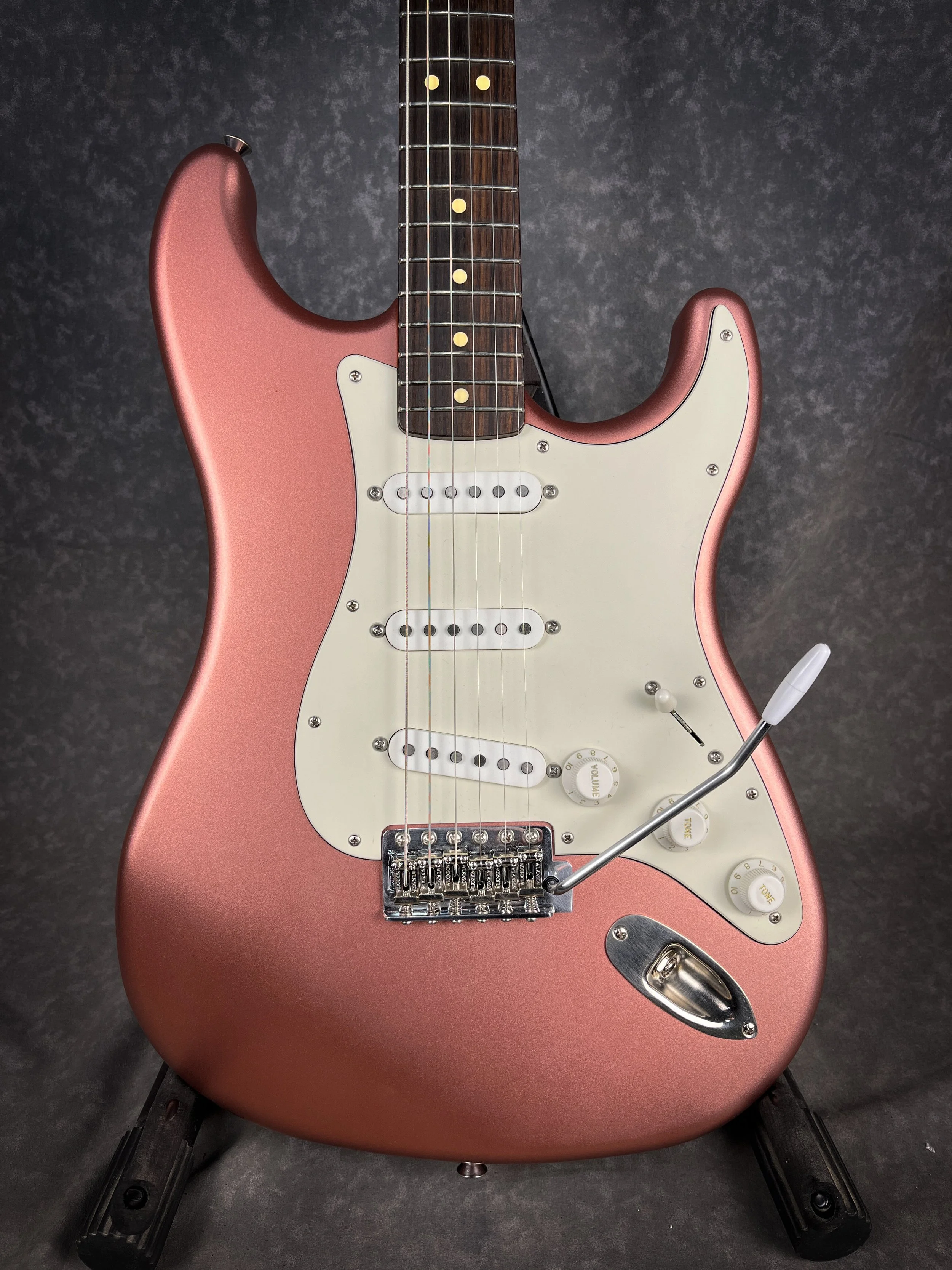 A Burgundy Mist LSL Saticoy  electric guitar with white pickguard, three single-coil pickups, and a whammy bar, set against a dark gray textured background.