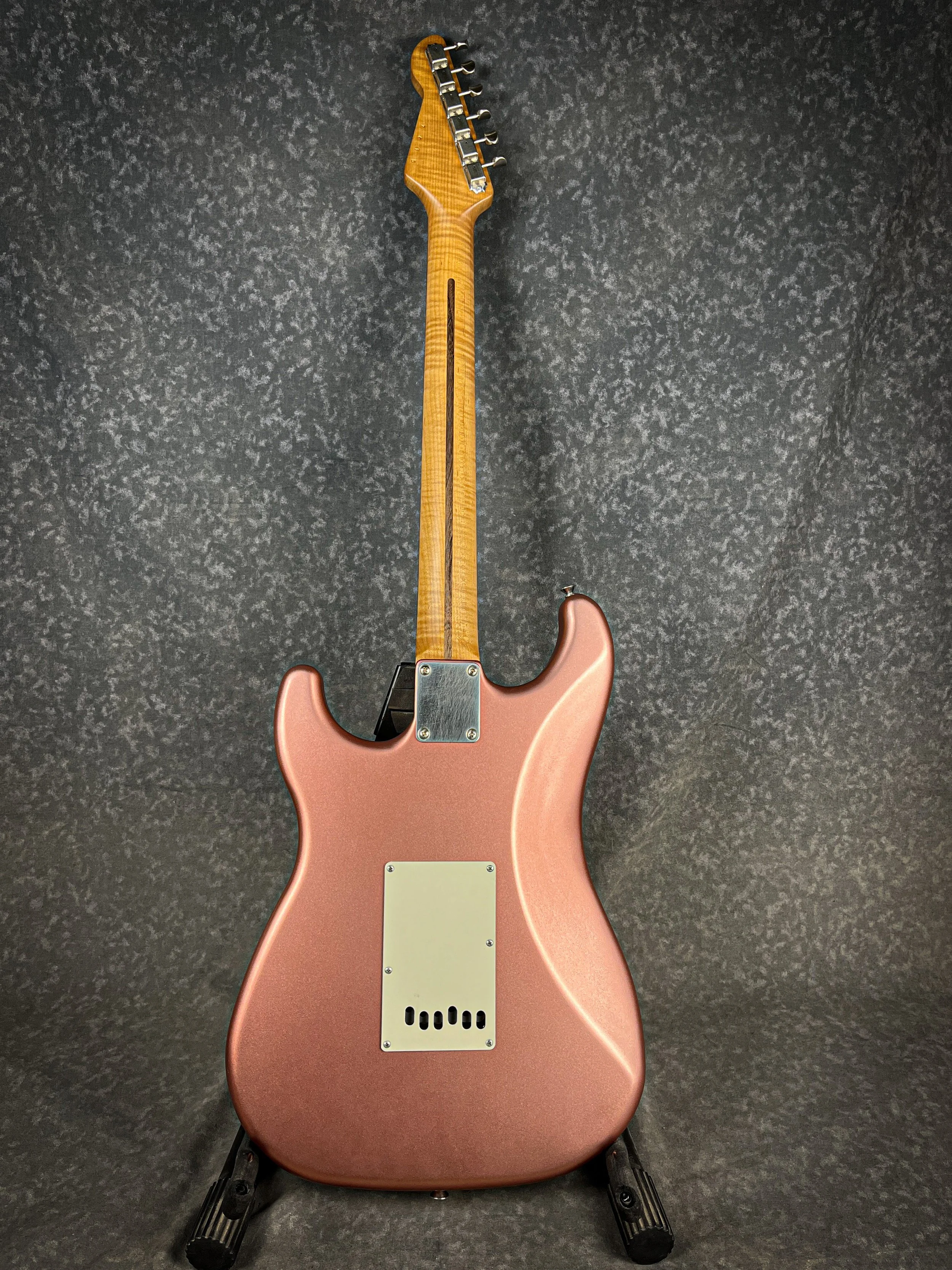 Back view of a Burgundy Mist LSL Saticoy  electric guitar with a wooden neck, resting on a black stand against a dark textured background.