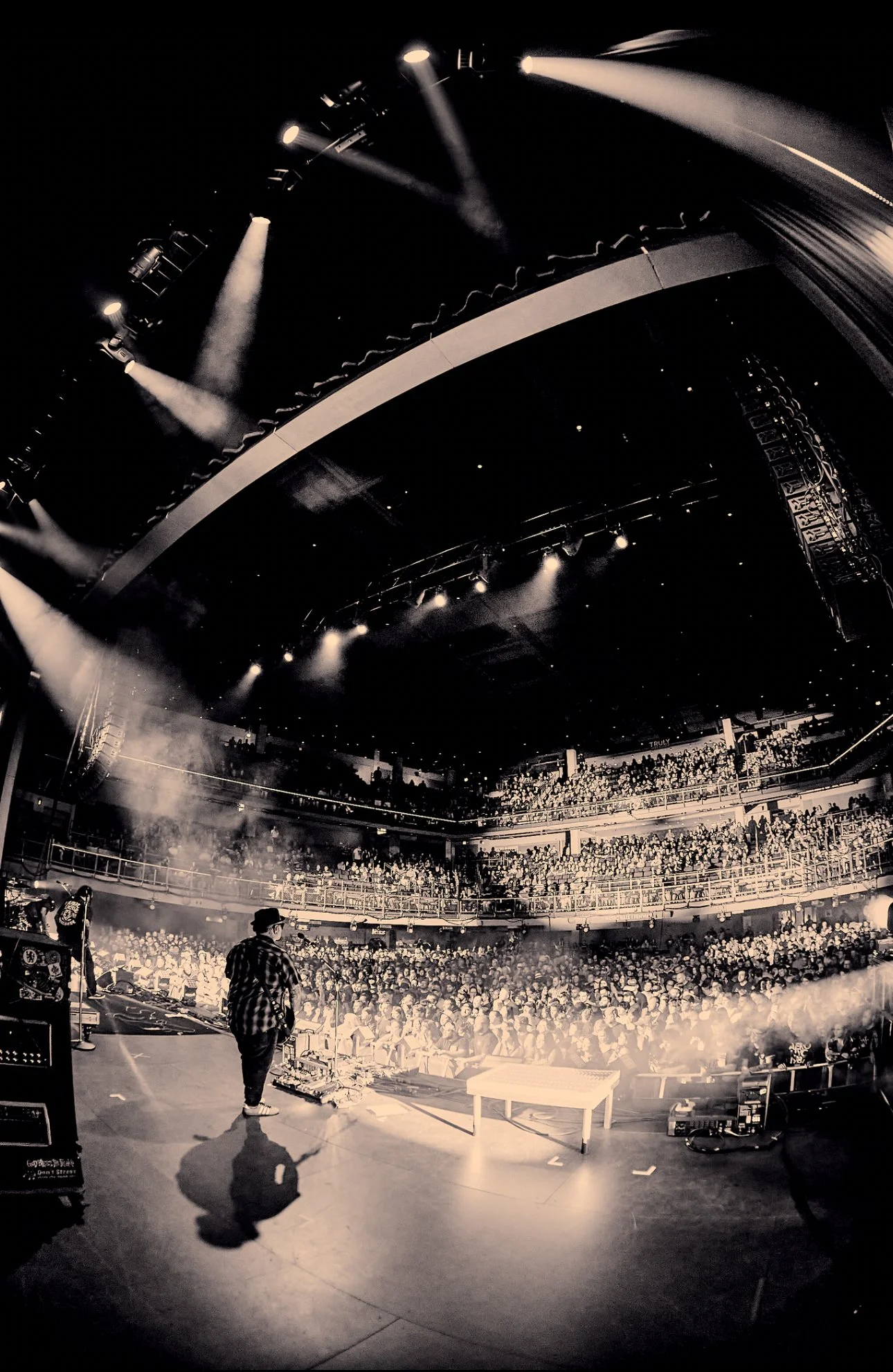 Black and white photo of a concert stage with Marcos Curiel and a large audience in a multi-level venue.