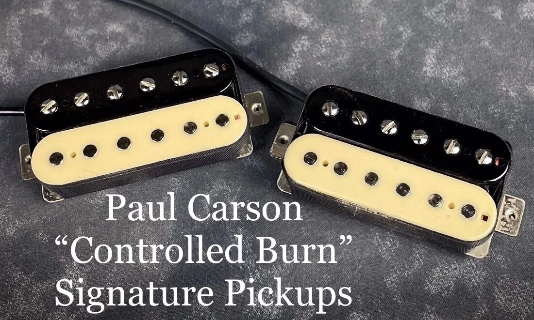 Two Paul Carson Revival guitar pickups with black and cream-colored covers, placed on a dark textured surface.