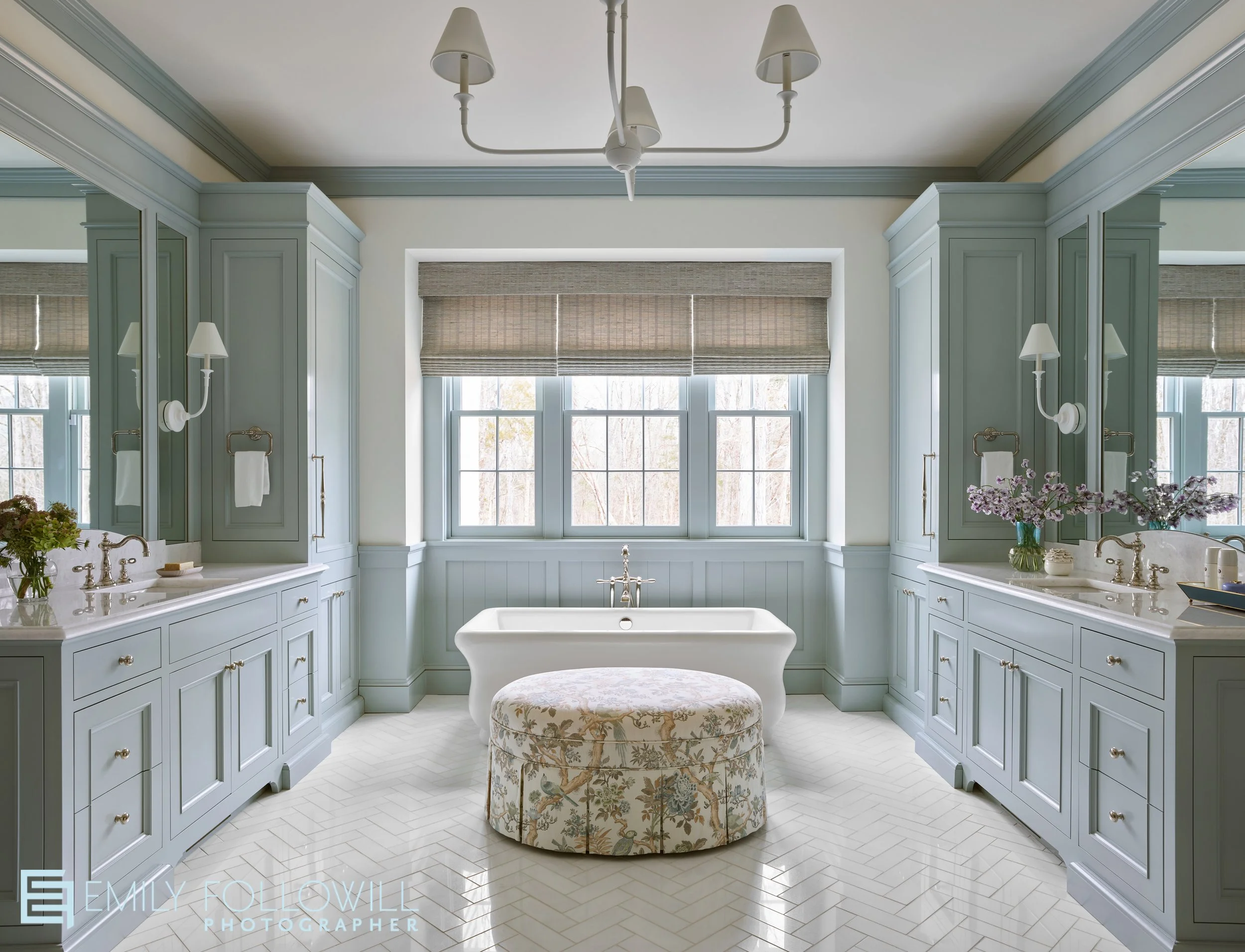 Large primary bathroom with green cabinetry surrounding the marble vanities. We look strait into the bathtub, which sits below a large window. Cabinetry by Kingdom Woodworks
