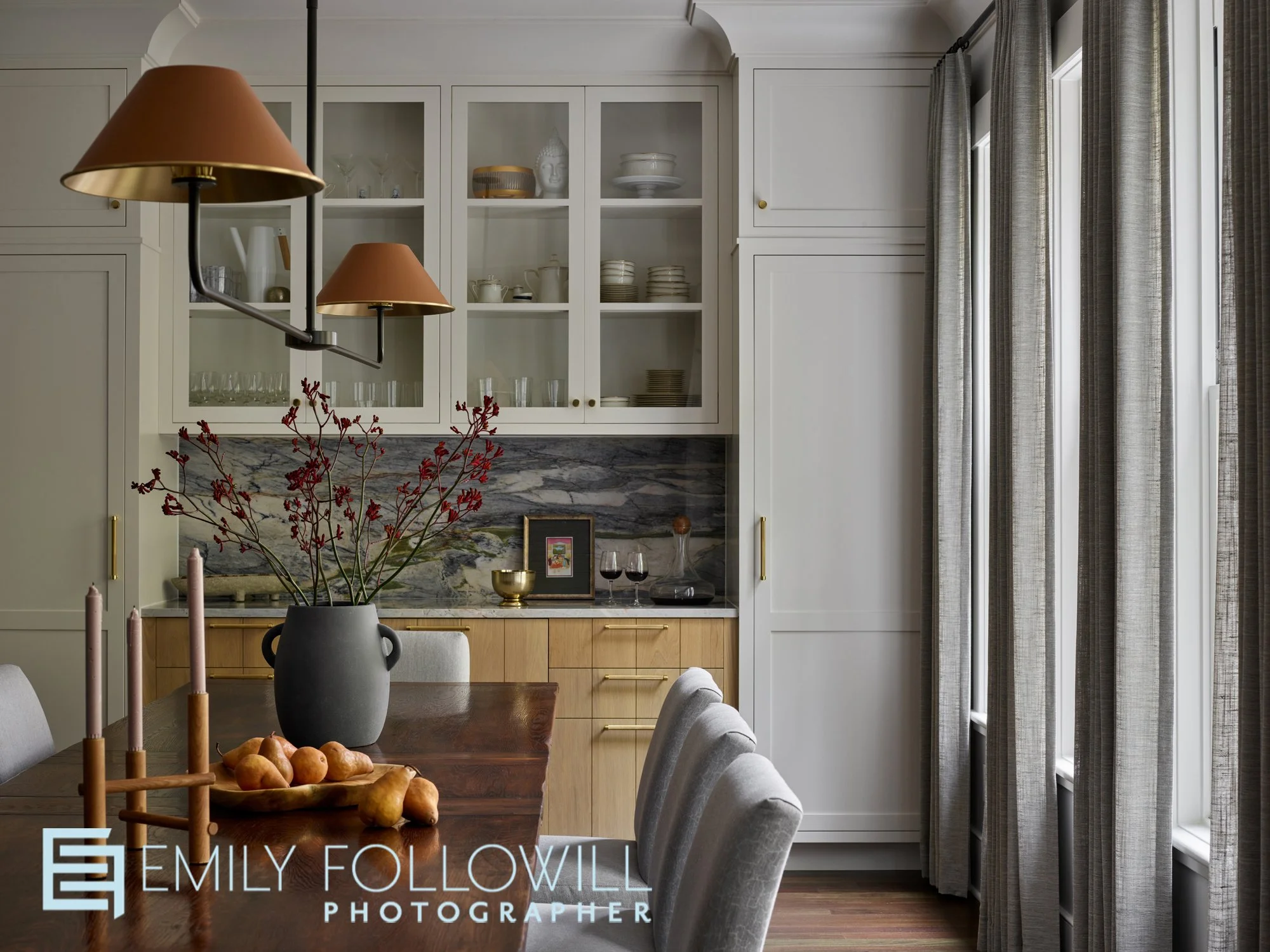 dining room table scape looking into the bar. Visual Comfort light fixture. grey drapery, candles and pears on the table. glass cabinetry in the bar, with a marble backsplash. located in Atlanta Ga