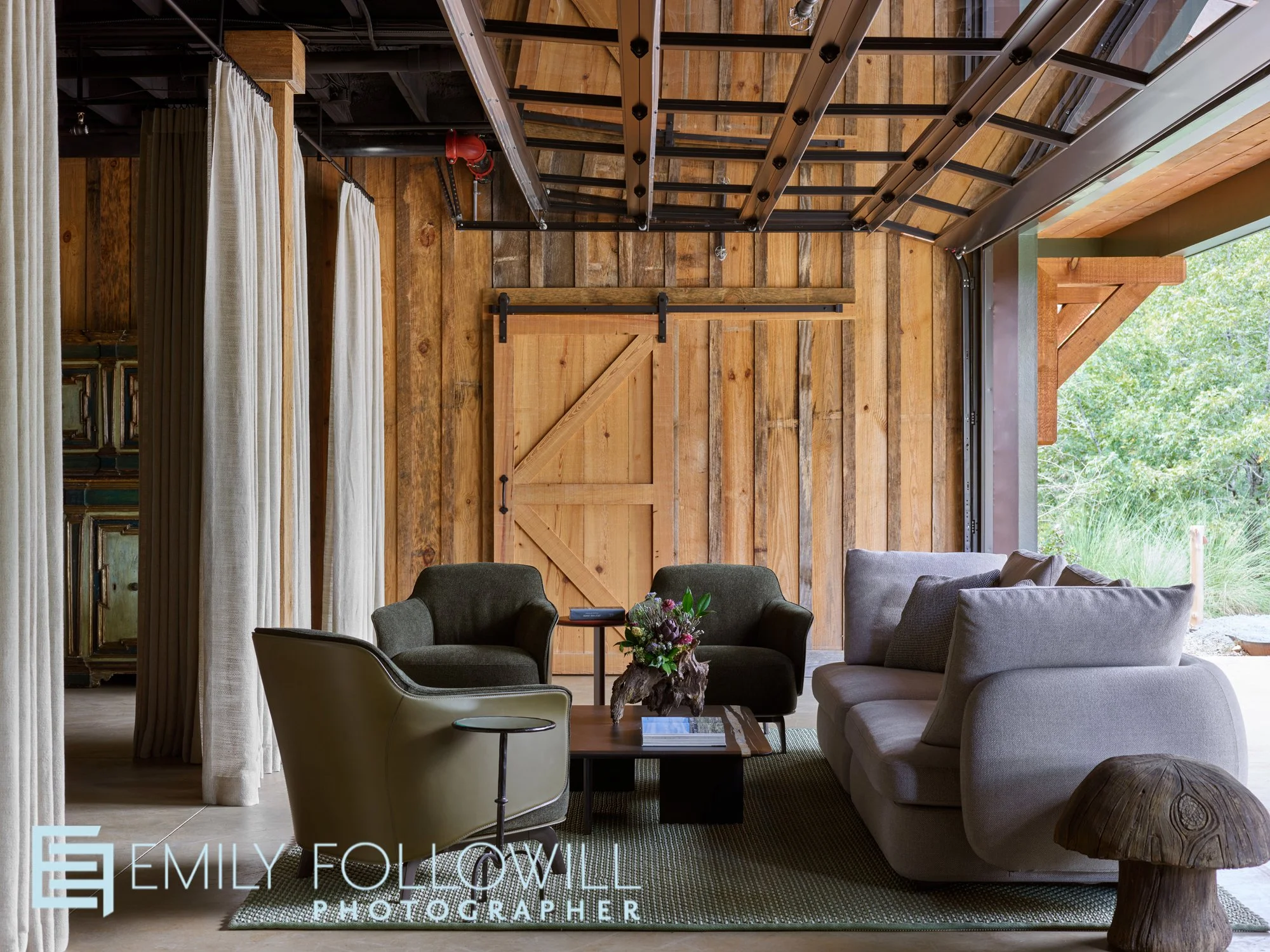 Barn style living space with rustic wooden walls, and a large garage door opening to the lush landscape outside.