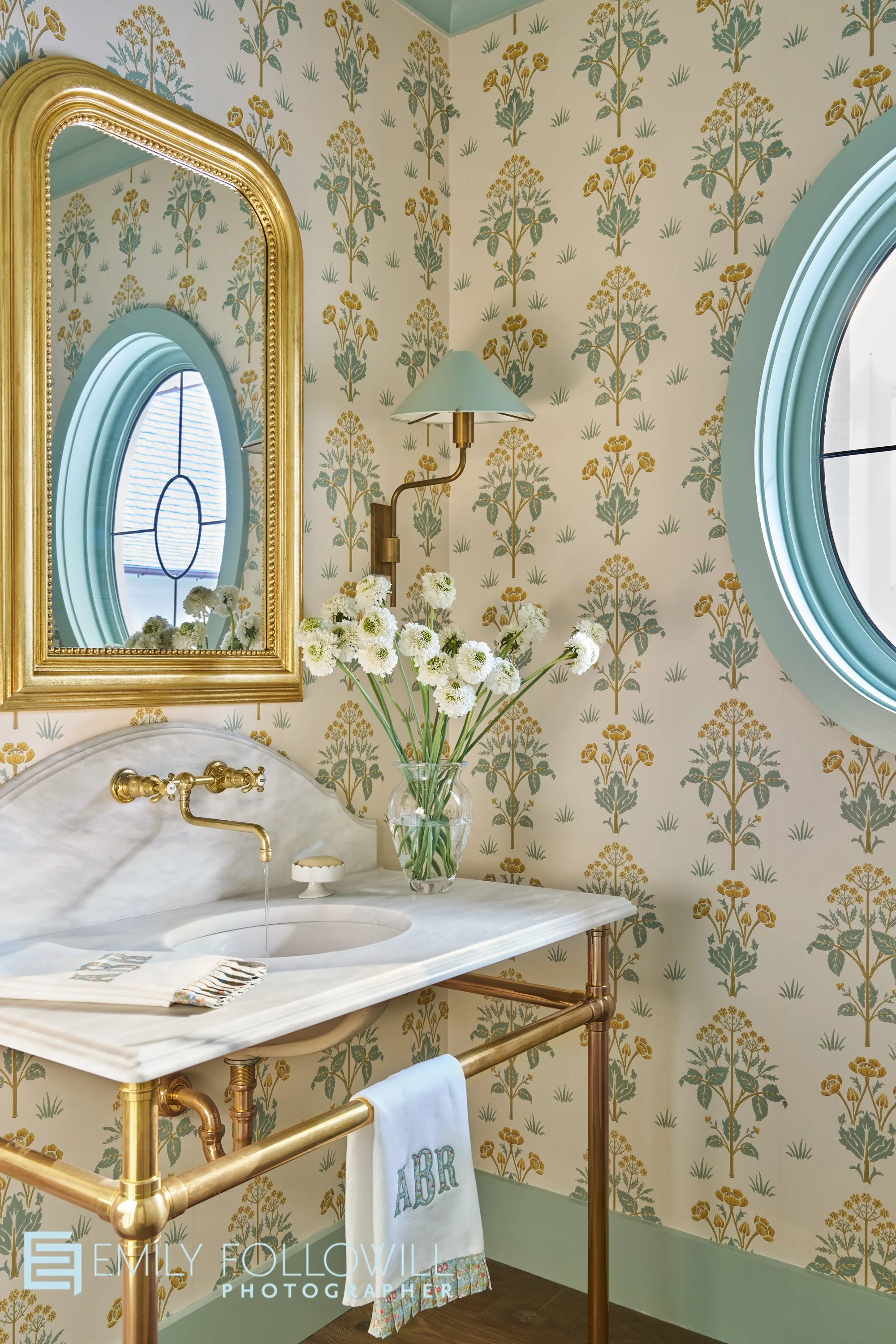 Bright, colorful powder room in Atlanta Georgia. An oval mirror is reflected in the large, ornate mirror hung over the marble sink with fixtures by Waterworks. Designed by Virginia Nocharli. Architect Greg Busch.
