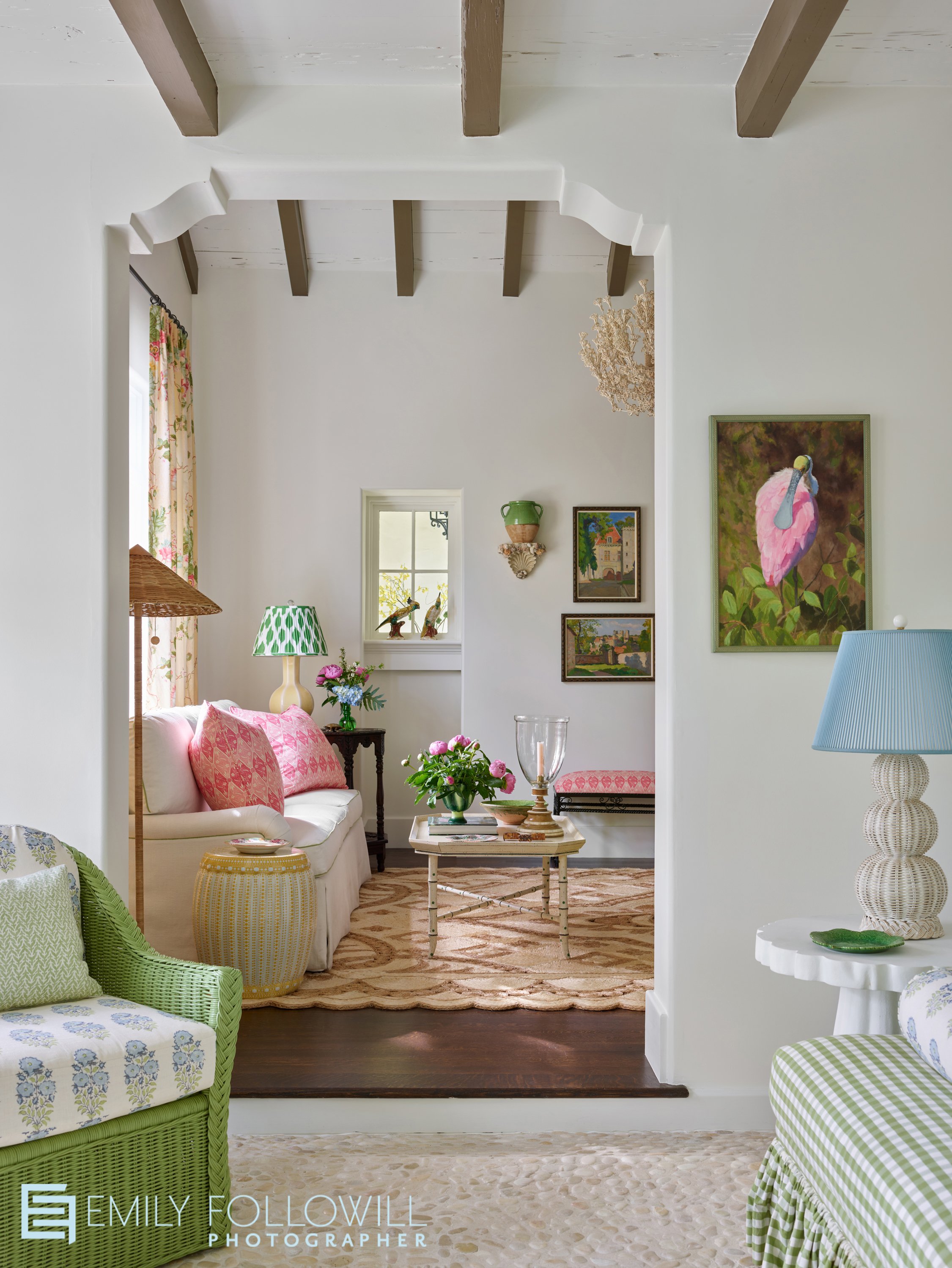 Bright, classic Sea Island Georgia Home. Shot from the sun room, looking into the living room through a carved doorway. Pops of pink compliment the green furniture. 