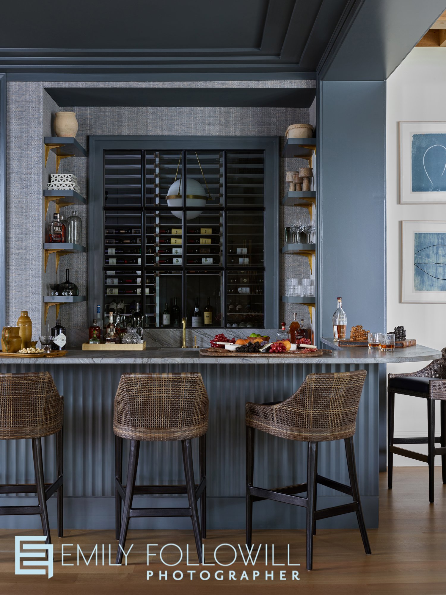 blue bar in a high end Lake Oconne vacation home. glass door showing the wine cellar. woven bar stools inviting guests to have a seat and enjoy a cocktail or glass of wine. 