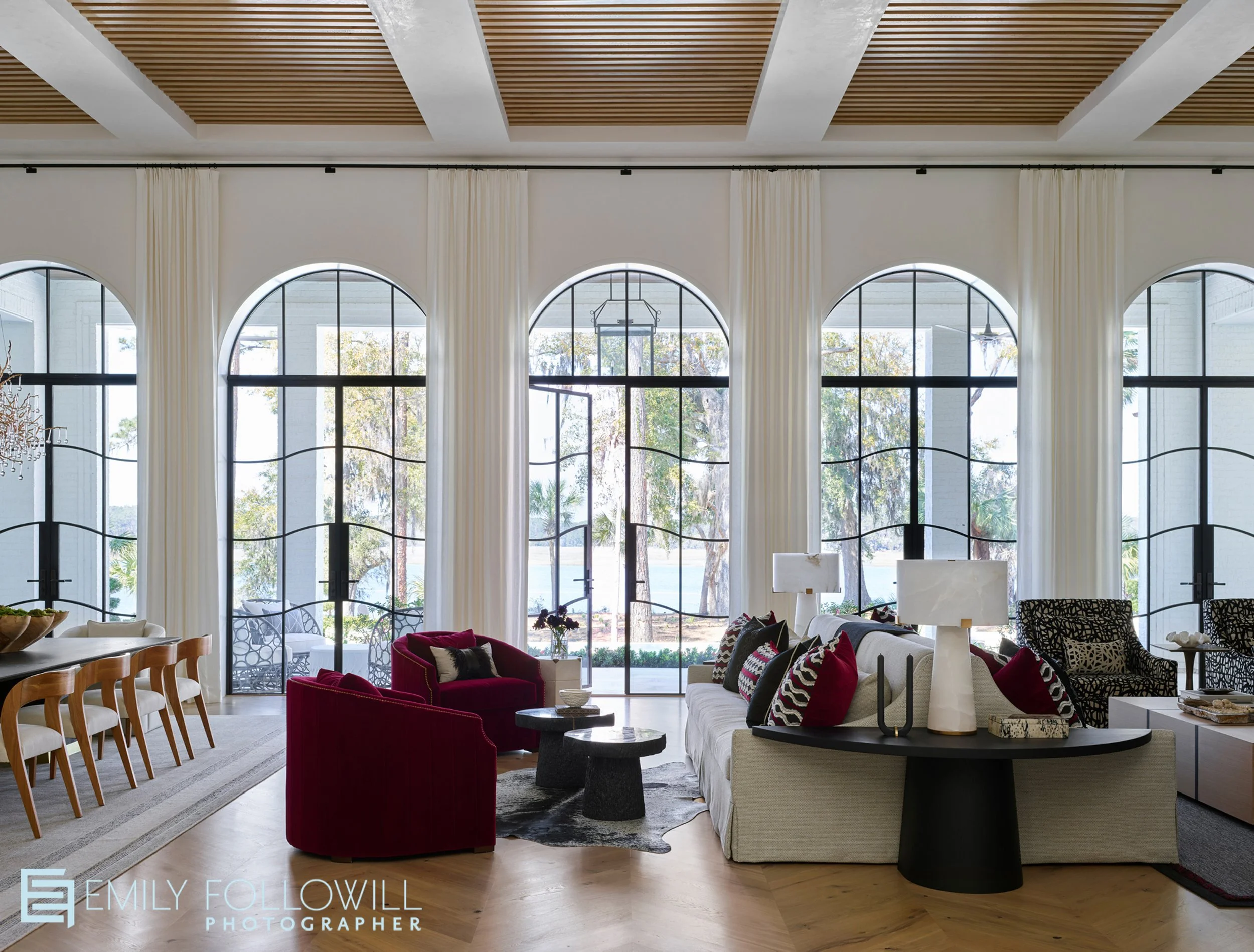 Large living room/ dining room with five arched iron doors overlooking the marsh in this Sea Island Georgia home. Designed by Abigail Interiors