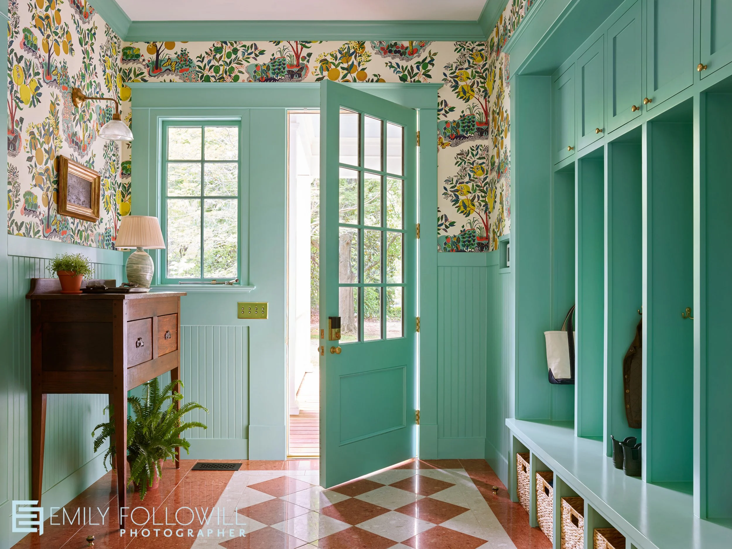 Bright teal green mudroom, with happy wallpaper. Orange and white checkered tile, with shelving to hang your coats, and put your shoes. Design by Lauren Elaine Interiors. Location; historic Inman Park in Atlanta Georgia