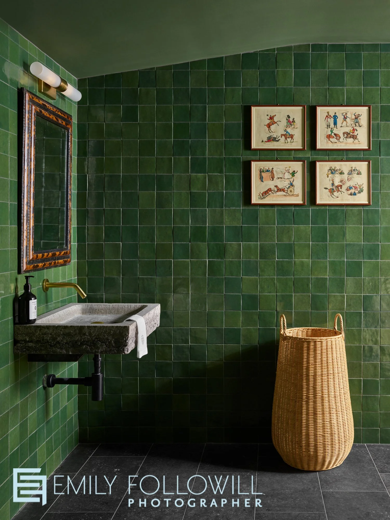 Green tiled powder room, with a basket underneath two small pieces of art.