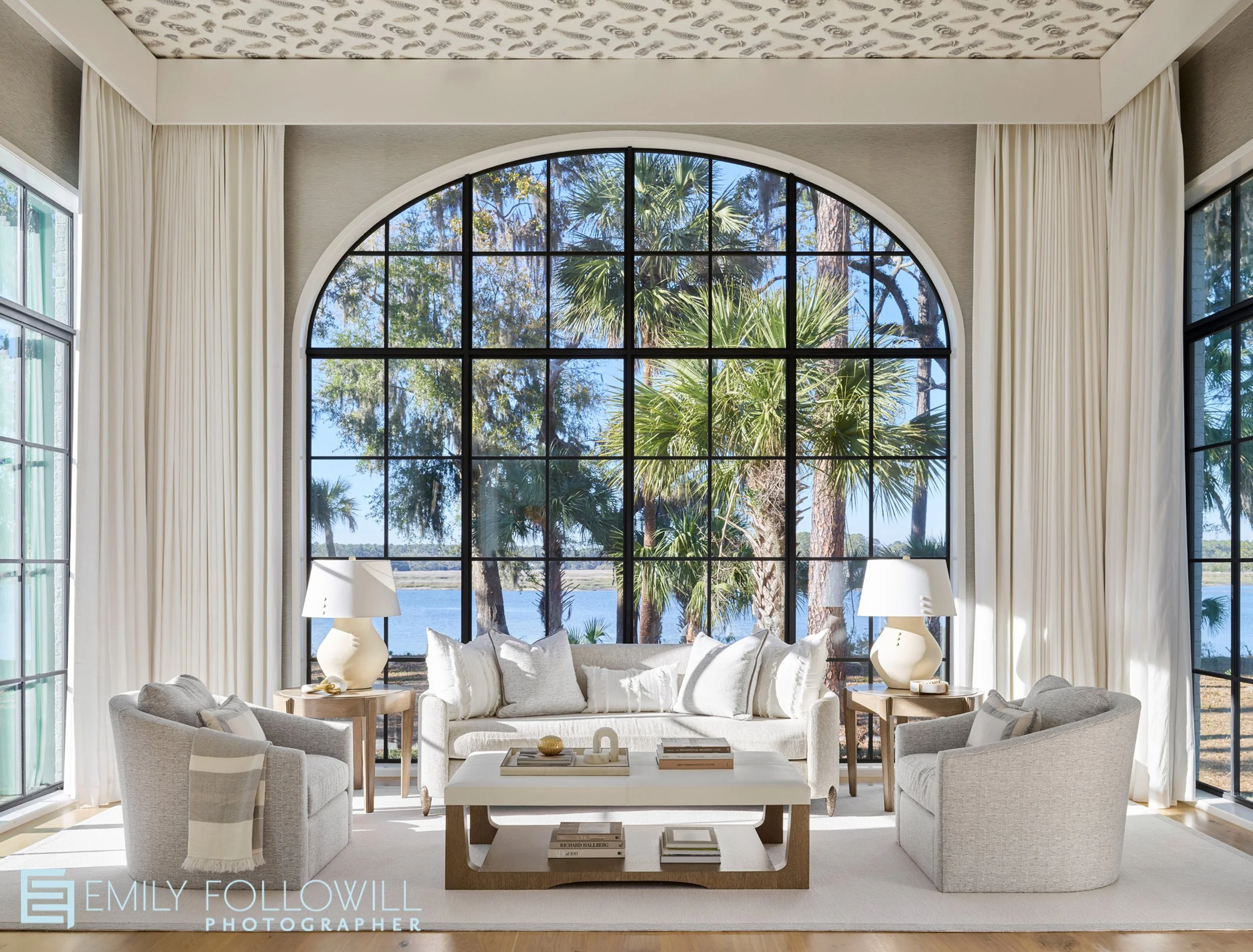 beautiful bright sitting area off of the primary bedroom.  Large Arched iron windows open to the view of the marsh in this Sea Island Georgia home. Design by. Abigail Interiors