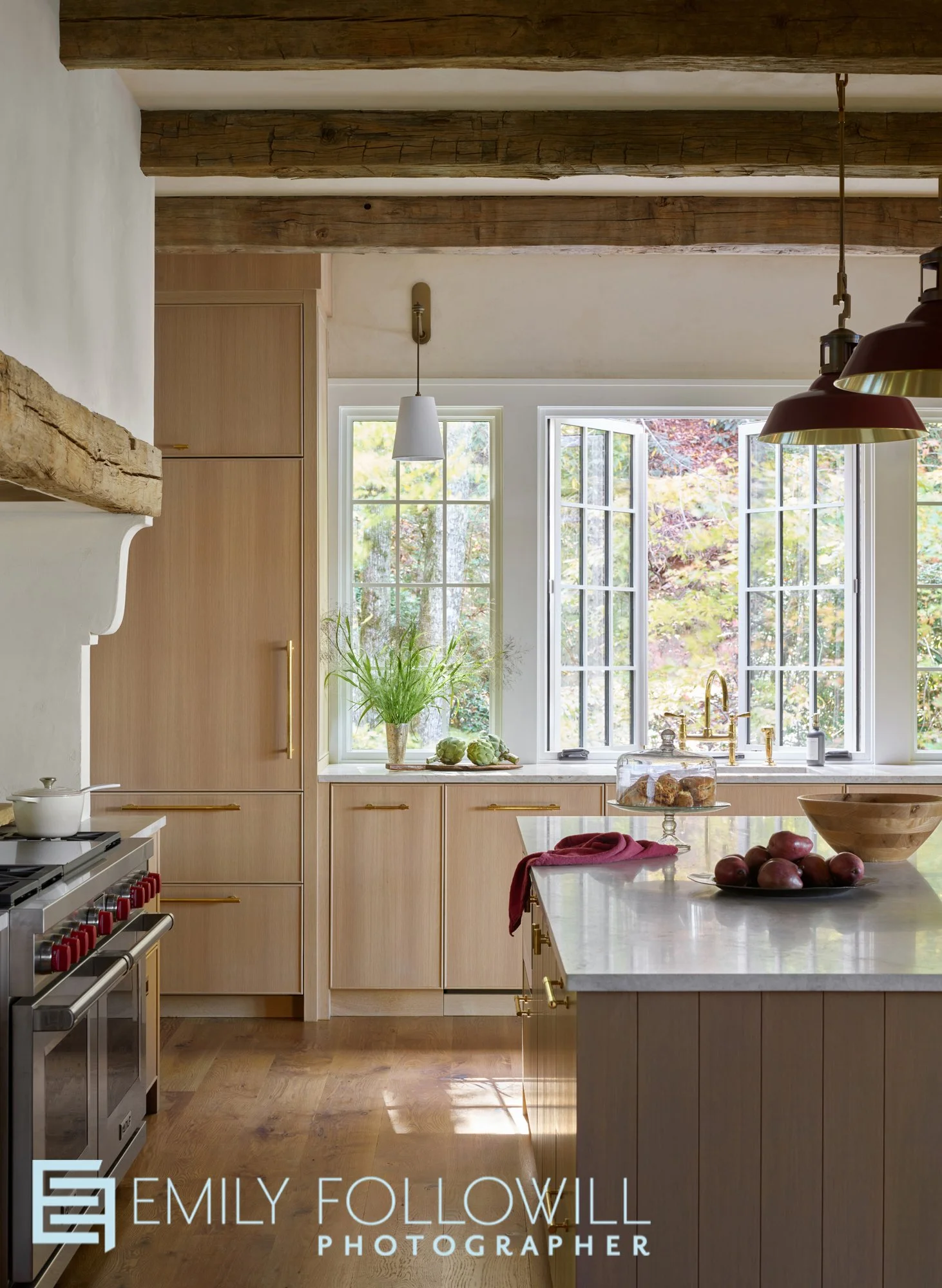 Lake house kitchen with wooden beams, a Wolf range, and a large island. Windows open above the Waterworks faucet, letting the fresh Lake Burton mountain air breeze through. Design by Melanie Milner