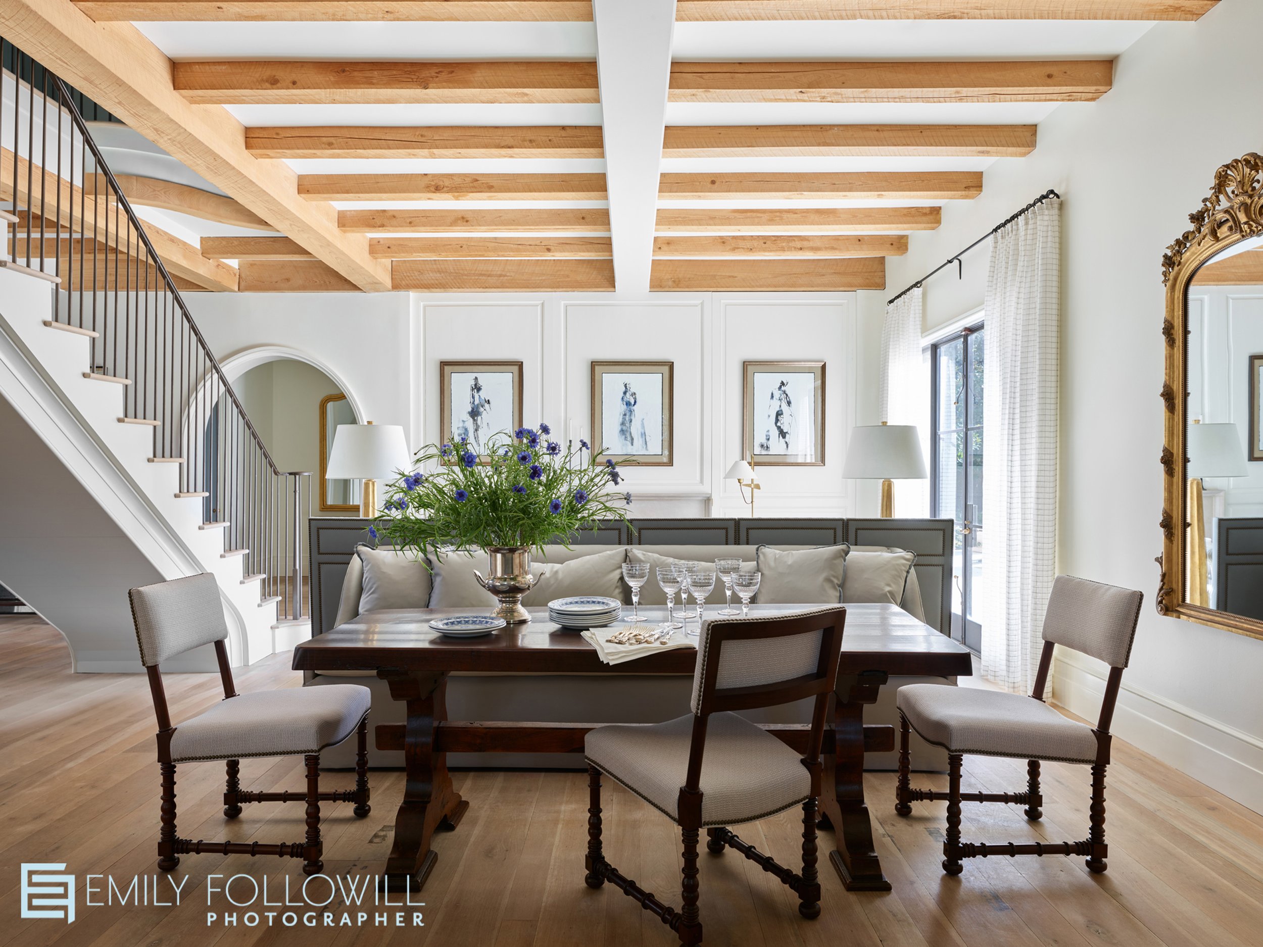 beautiful dining room open to the living room and staircase leading upstairs. White walls, wooden beams, arched doorways and a gold mirror. located in Montgomery Alabama. Designed by Ashley Gilbreath
