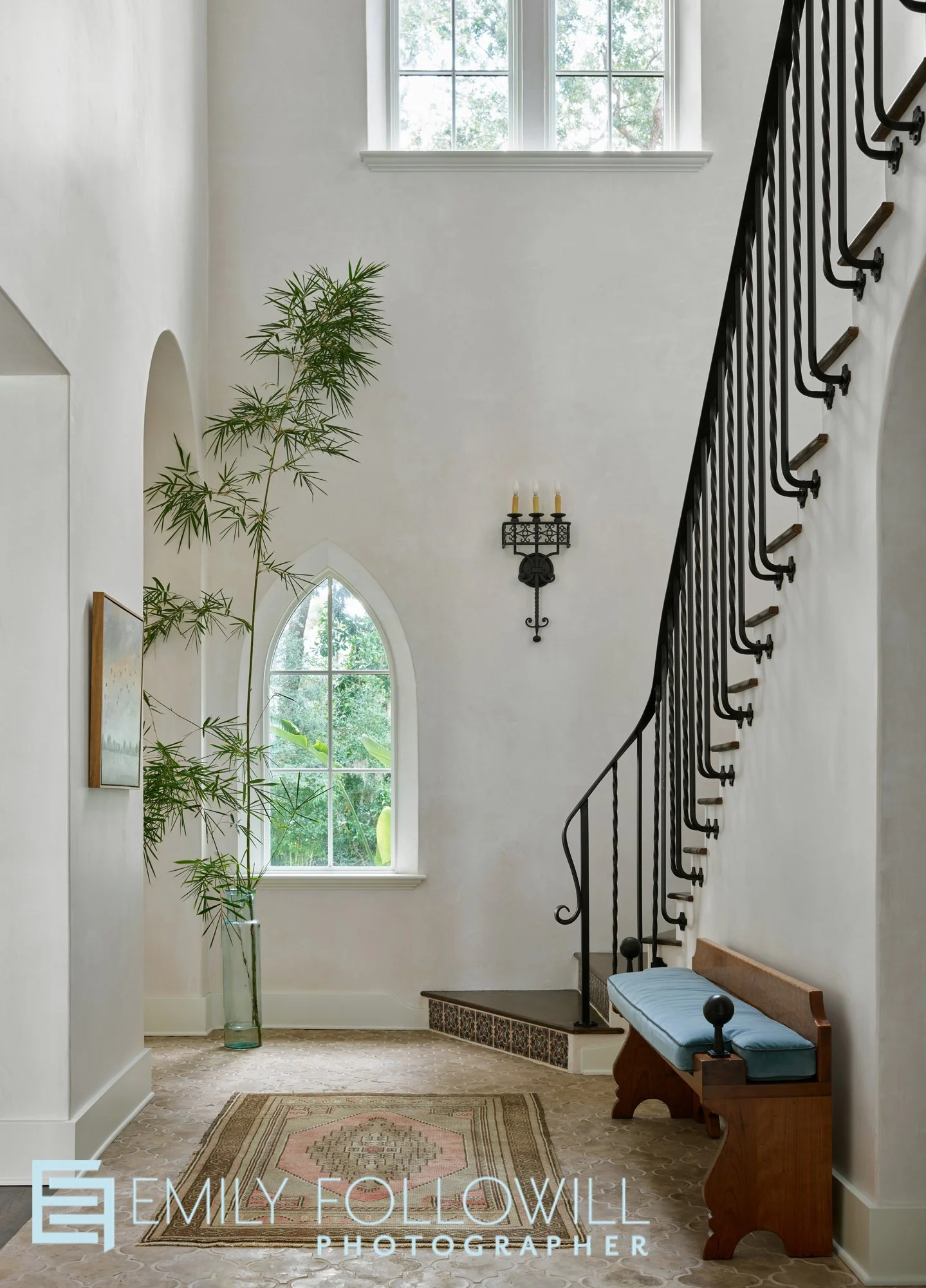 Dramatic, spanish style hallway with an iron rod staircase leading of the second floor. An arched window shows views of the palm trees in this Sea Island Georgia home. Design by Courtney Giles Interiors