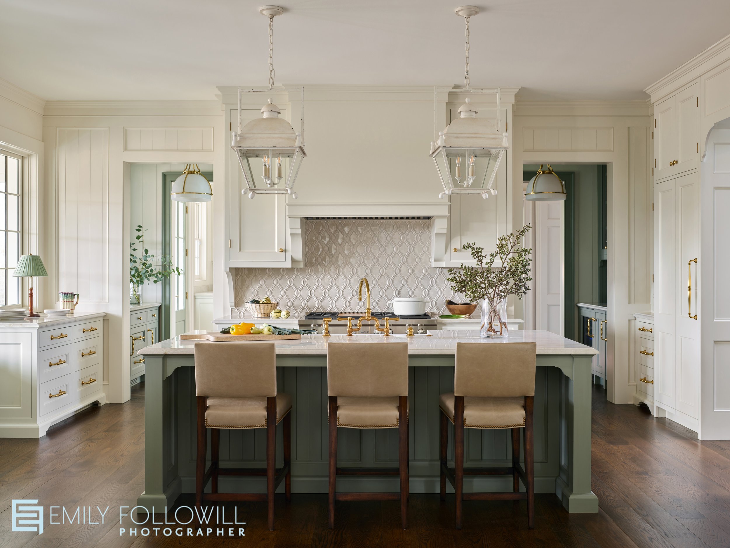 Large kitchen looking strait into the green wooden island topped with marble. The tiled backsplash surrounds the cooking range. Cabinetry Design by Kingdom Woodworks.
