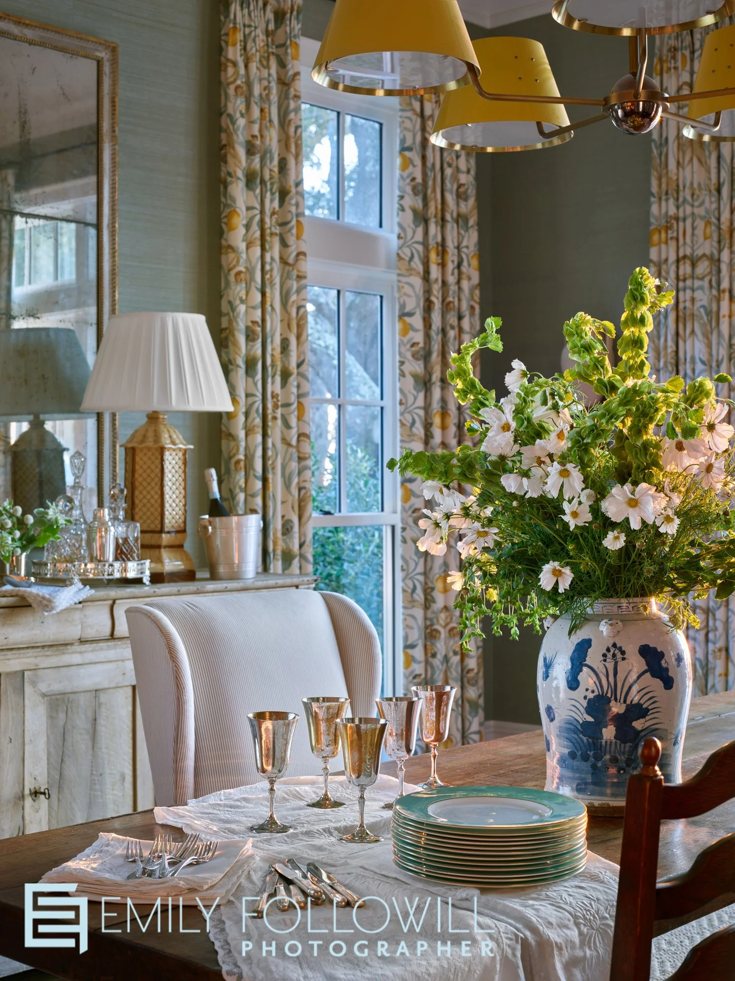 A detail photo in a green dining room. Bright wildflowers illuminated by the afternoon light. Silver wine glasses ready to serve guests. Location : Fairhope Alabama. Design by Ashley Gilbreath