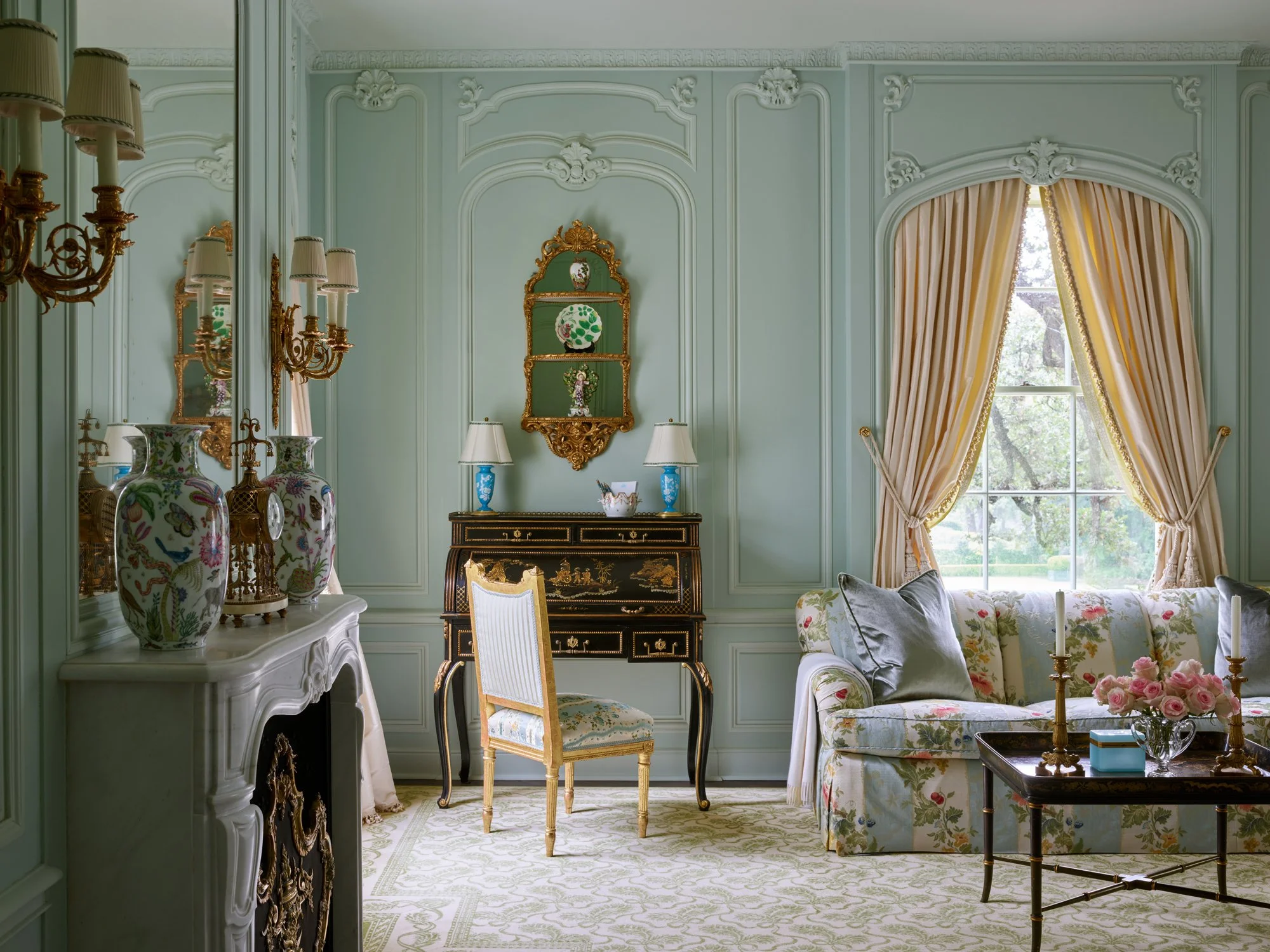 ornate carved wooden walls painted a light green. Cream drapery hangs between the arched winodw. Location: Texas