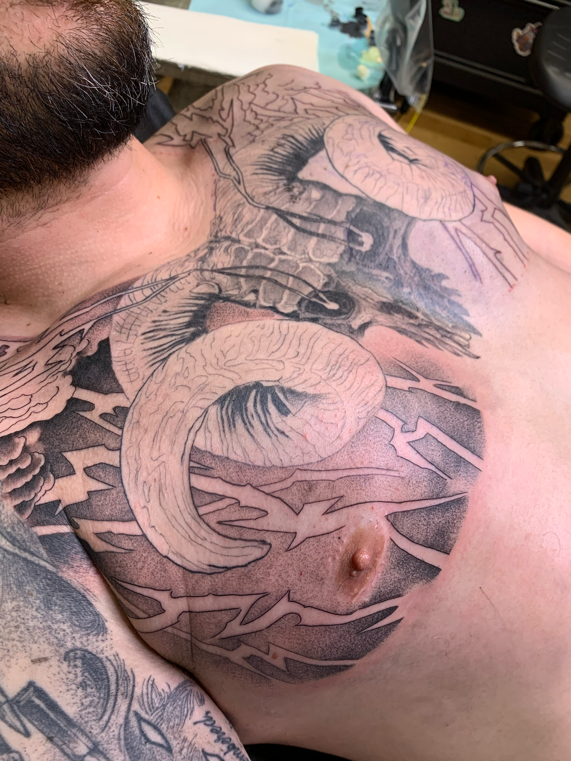 A tattoo being inked on a person's chest, featuring a detailed snake intertwined with lightning bolts and cloud-like clouds.