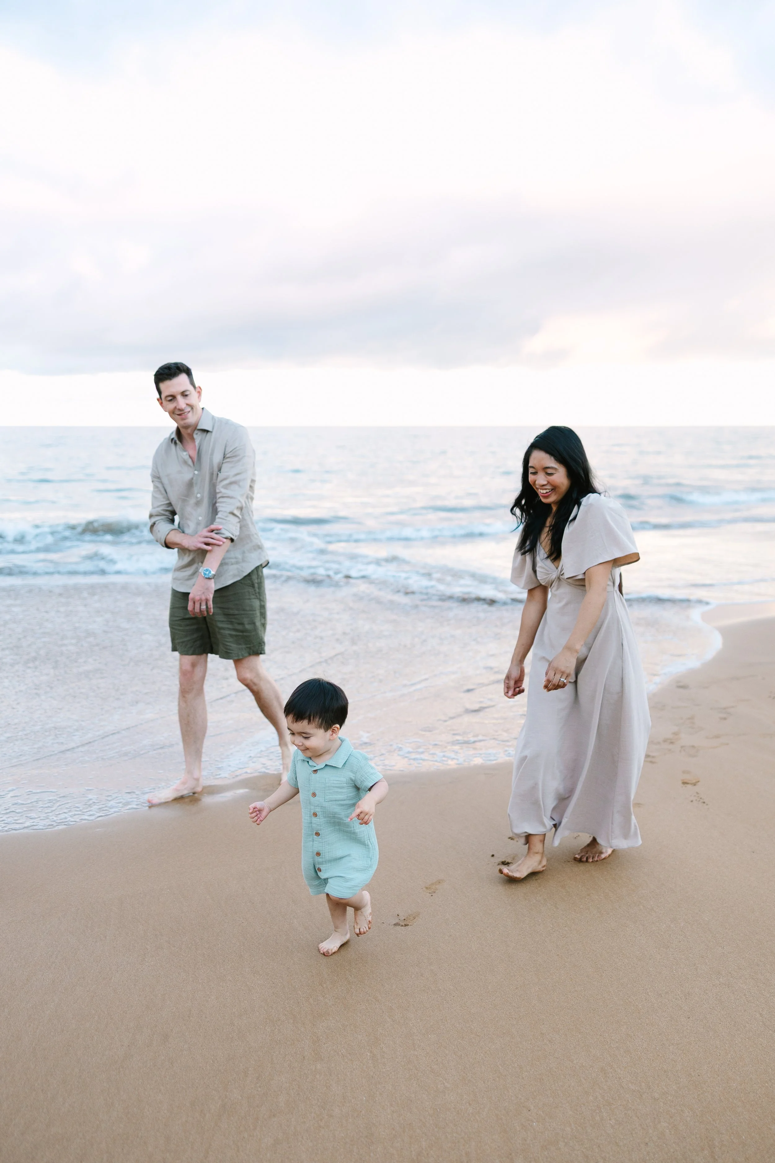 A group of four people, including two adults and two children, walking on the beach near the ocean. The sky is cloudy, and they appear to be enjoying a casual stroll by the water.