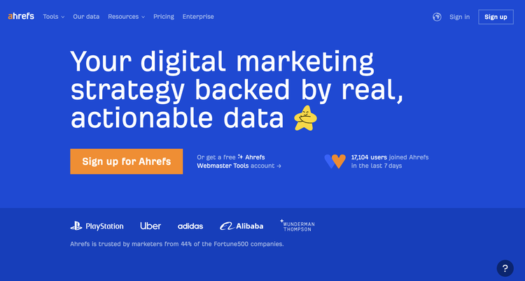 Screenshot of Ahrefs website homepage with blue background, white text, orange sign-up button, and logos of PlayStation, Uber, Adidas, Alibaba, and Wonderman Thompson.