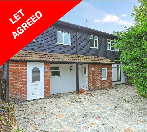 Two-story townhouse with a brick and blue siding exterior, front door, and stone driveway, with a green tree on the right.